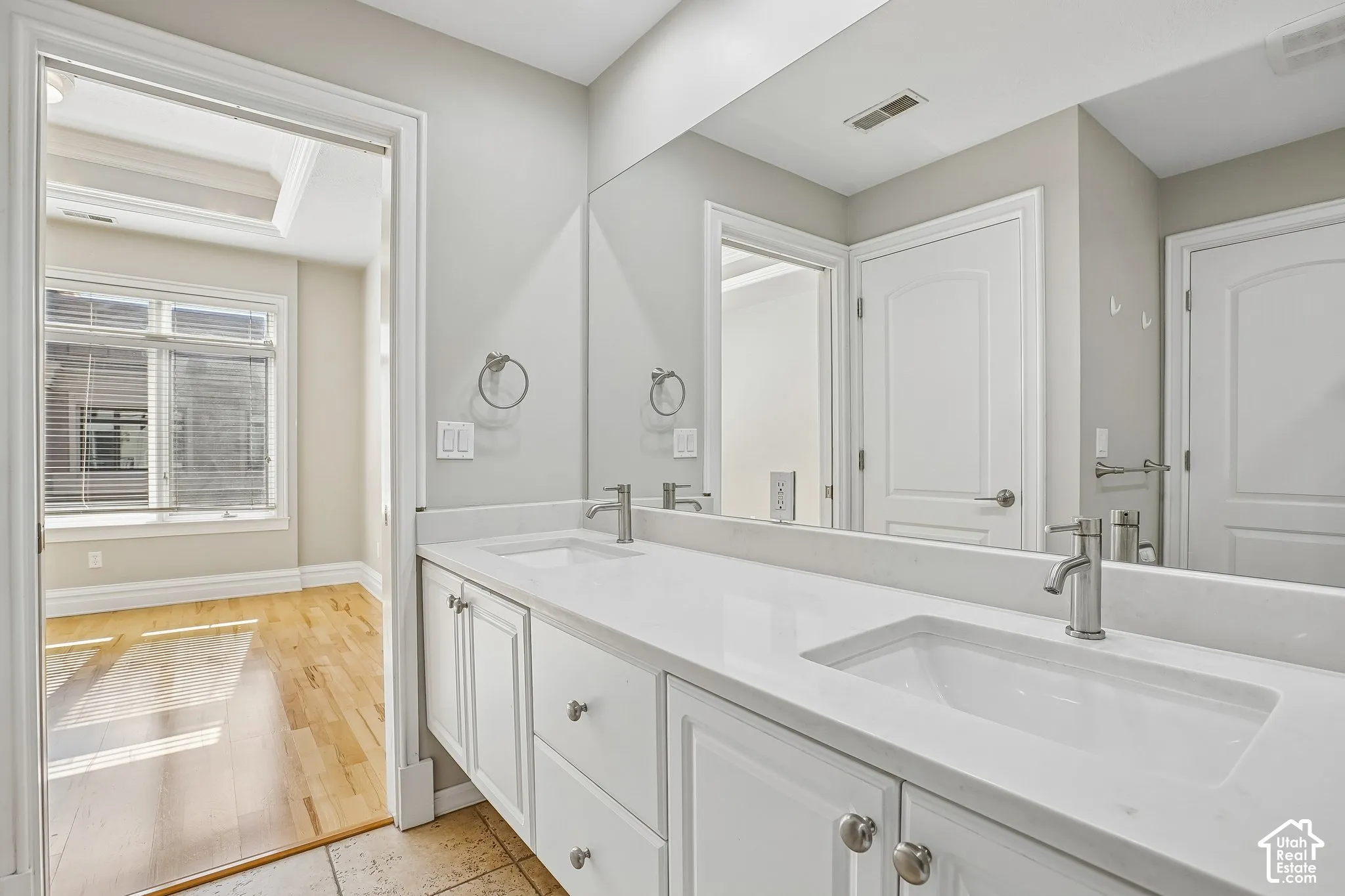 Dual-sink vanity with white cabinetry, light-toned stone-style countertop, undermount sinks, and brushed-nickel faucets, complemented by a large wall-mounted mirror