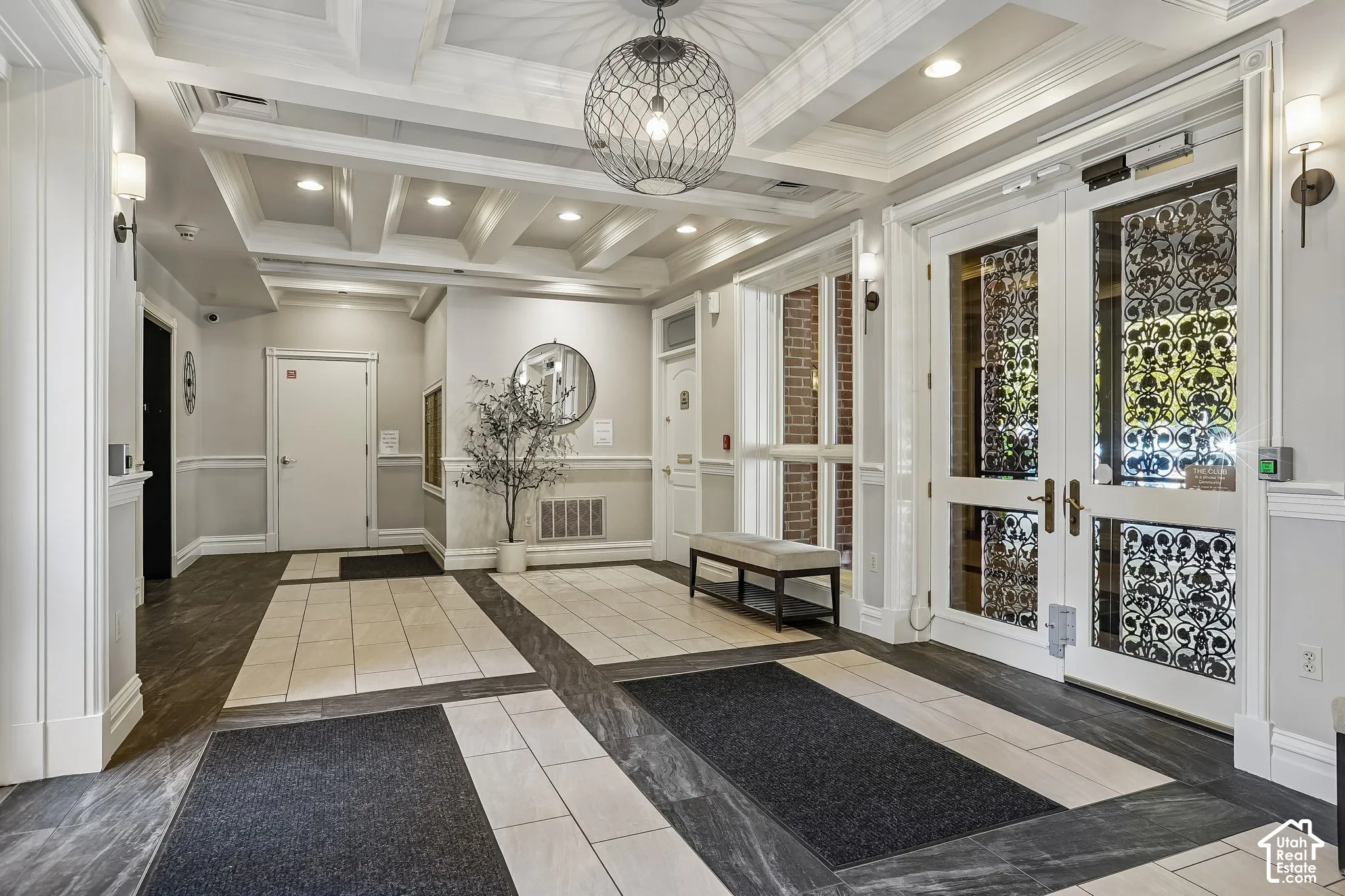 Grand foyer featuring decorative wrought iron-style door glass, coffered ceilings with recessed lighting, a statement orb chandelier, and tile flooring with stone-finish inlays
