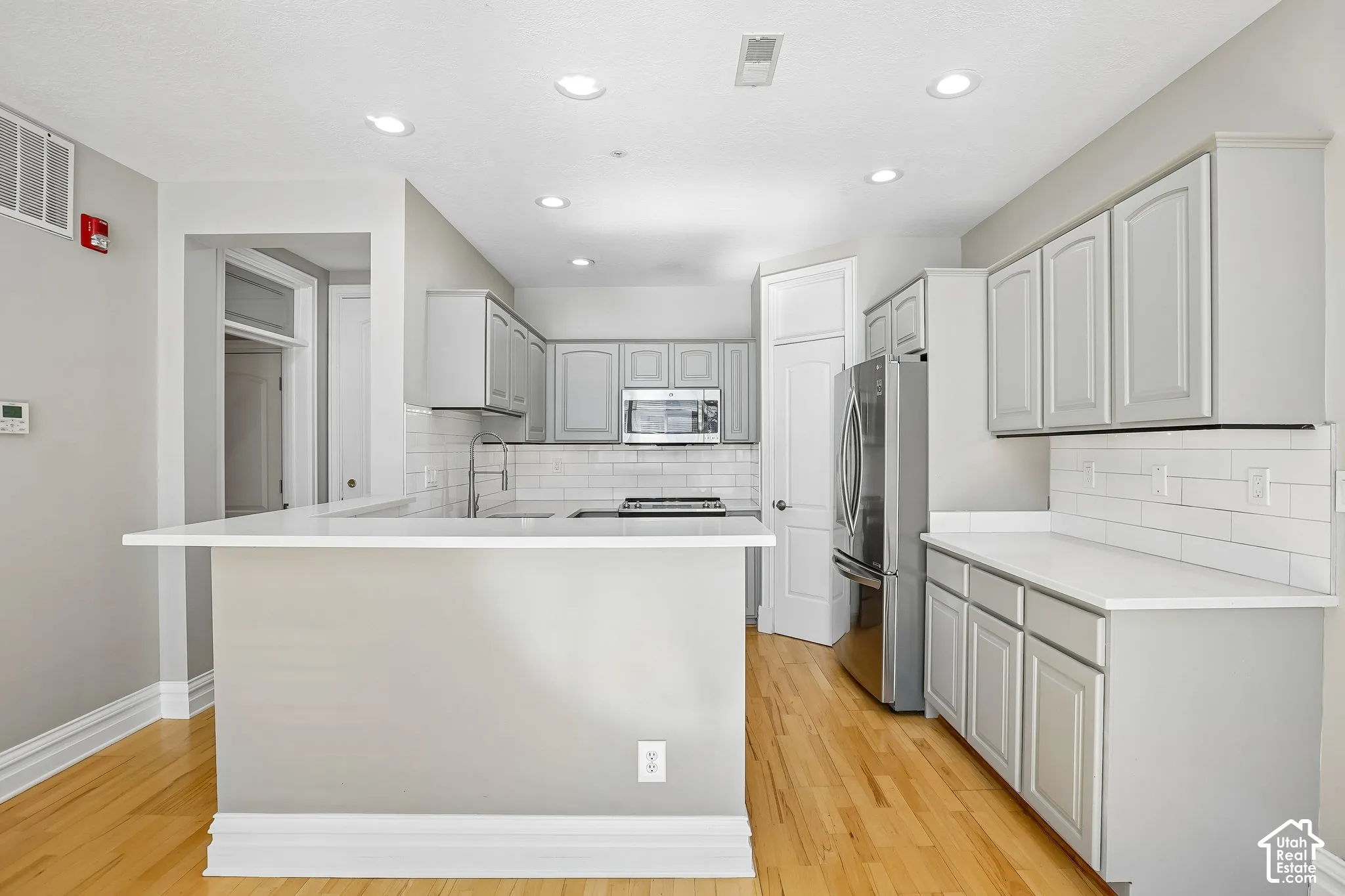 Kitchen featuring light grey shaker-style cabinetry, white countertops, subway tile backsplash, recessed lighting, and wood-finish flooring