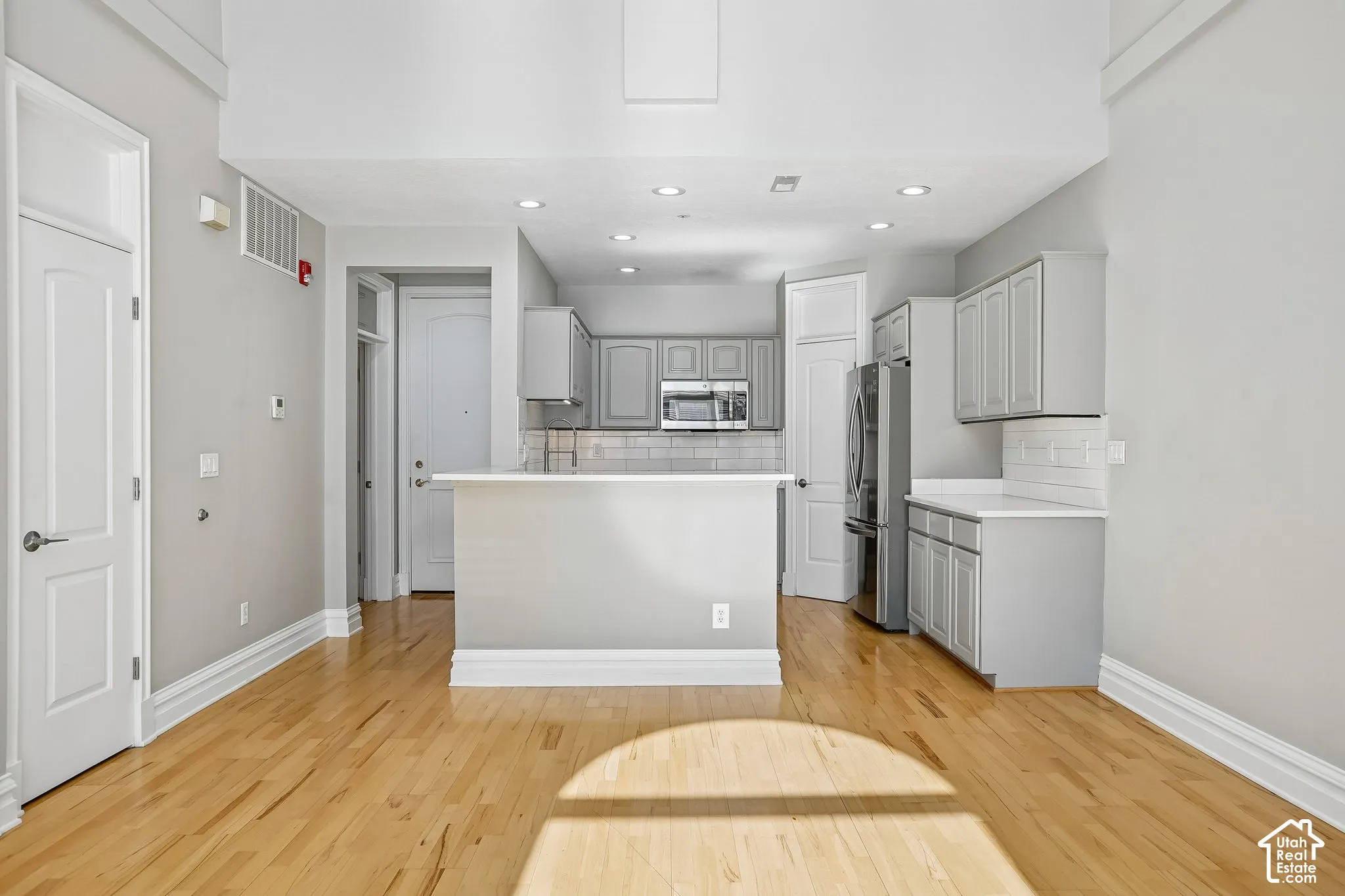 Kitchen featuring wood-finish flooring, shaker-style cabinetry, a peninsula with a white countertop, and subway tile backsplash