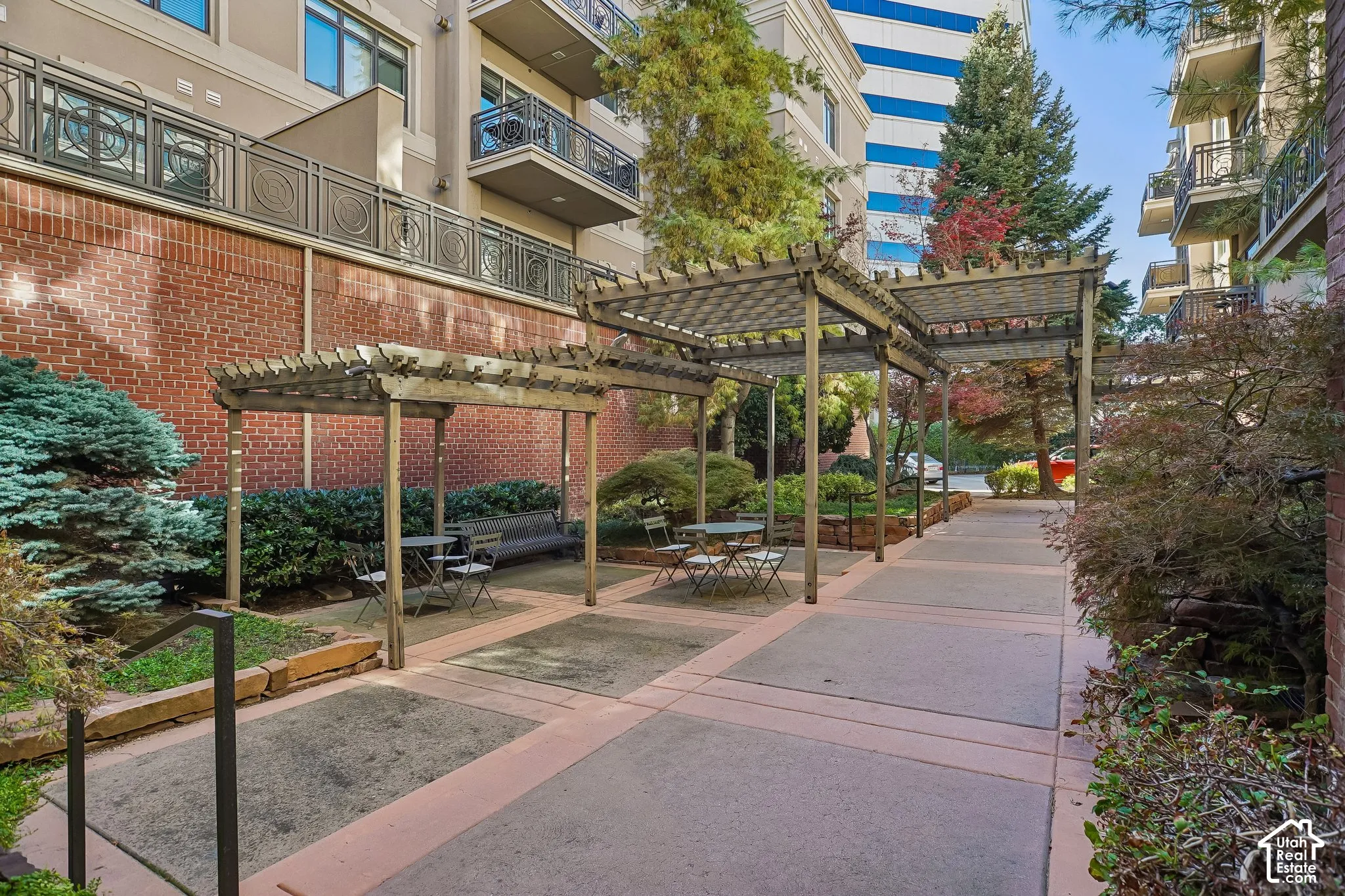 Common area featuring concrete pathways, two wooden pergolas, brick retaining walls, and mature landscaping
