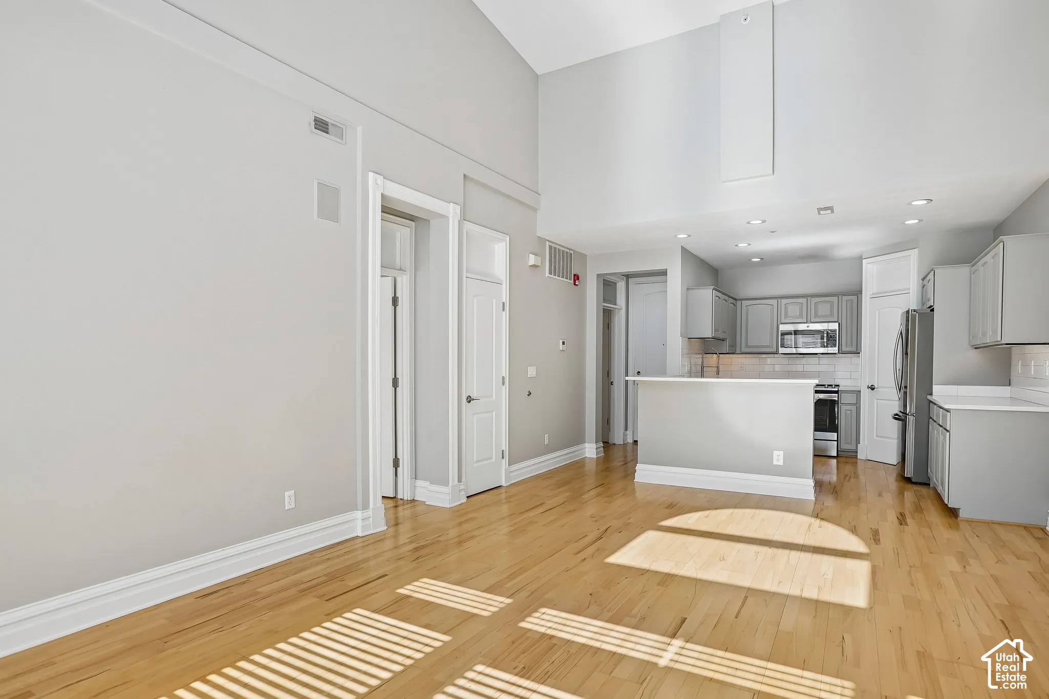 Vaulted ceilings, wood-finish flooring, kitchen peninsula, recessed lighting, and crisp neutral-tone cabinetry