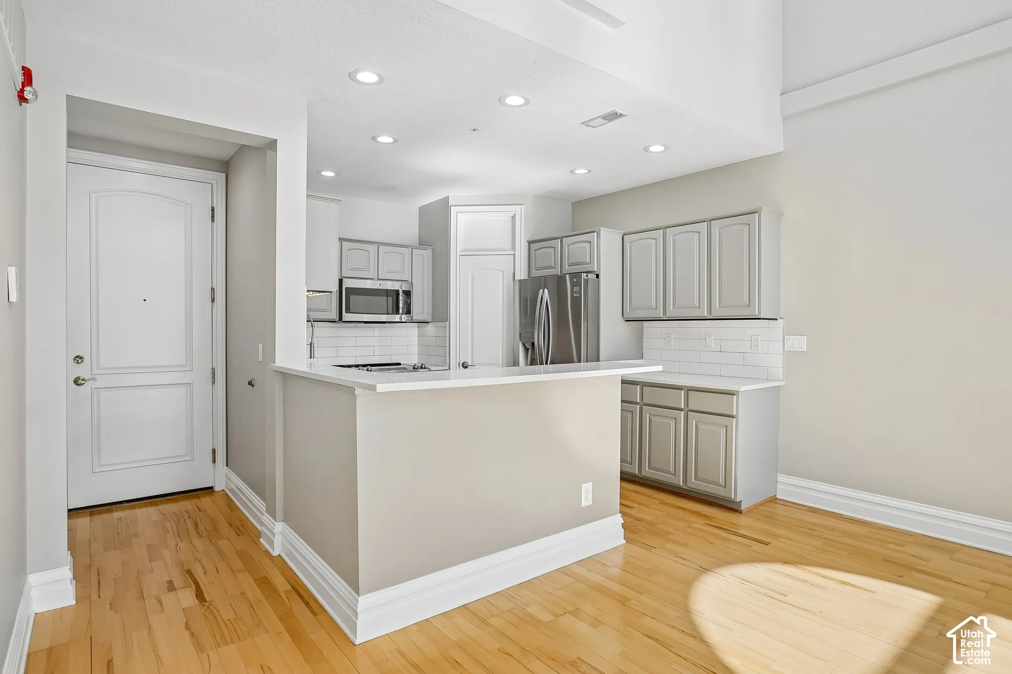 Kitchen featuring grey cabinetry, white subway tile backsplash, solid-surface countertops, wood-finish flooring, and recessed lighting