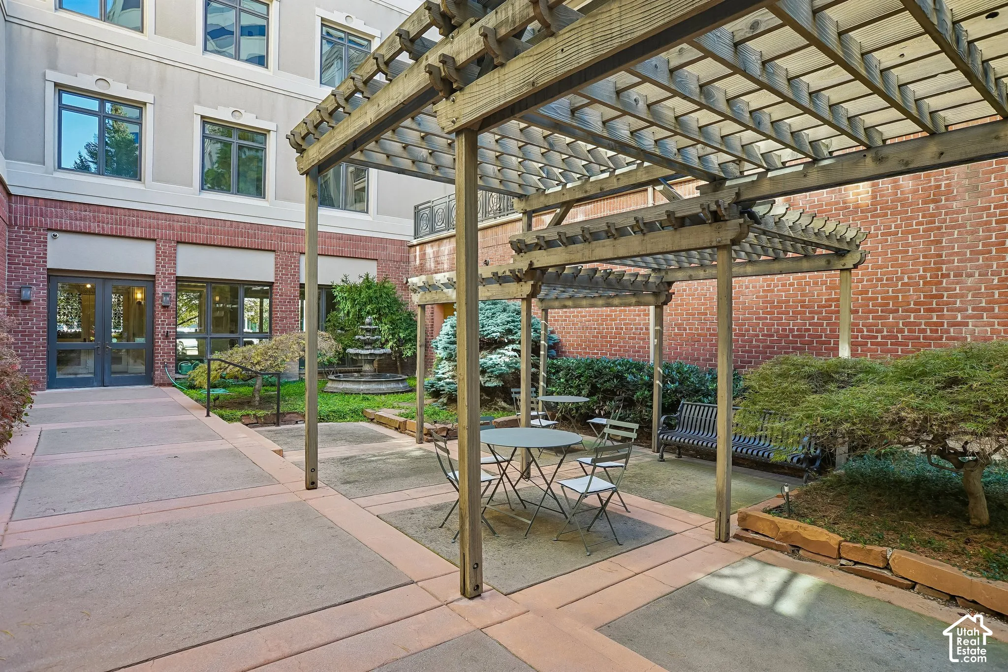 Outdoor courtyard featuring a wood pergola, concrete patio, ornamental fountain, and structured landscaping