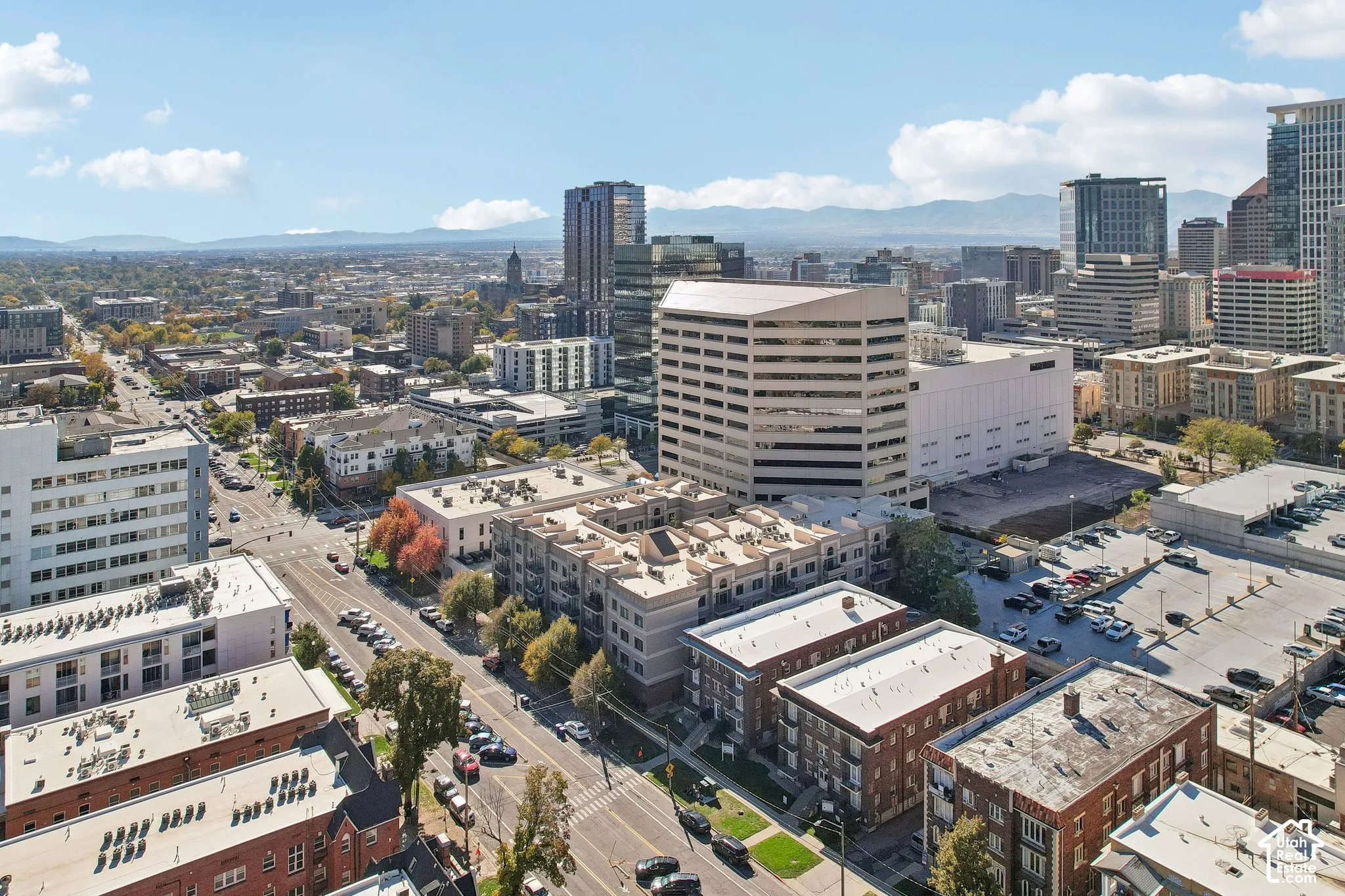 Aerial perspective of an urban setting featuring a high-density cityscape, multi-story masonry structures, surface parking, and a backdrop of mountain ranges