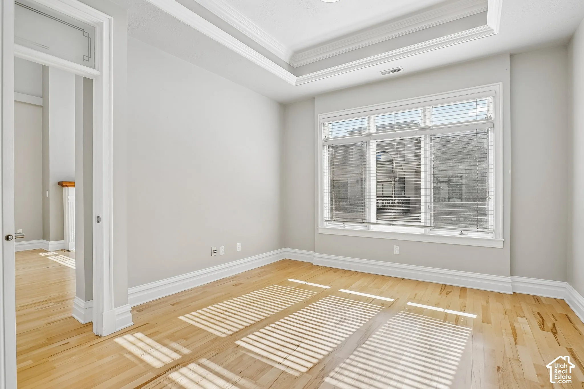 Room featuring tray ceilings, wood-finish flooring, and large windows with integrated blinds