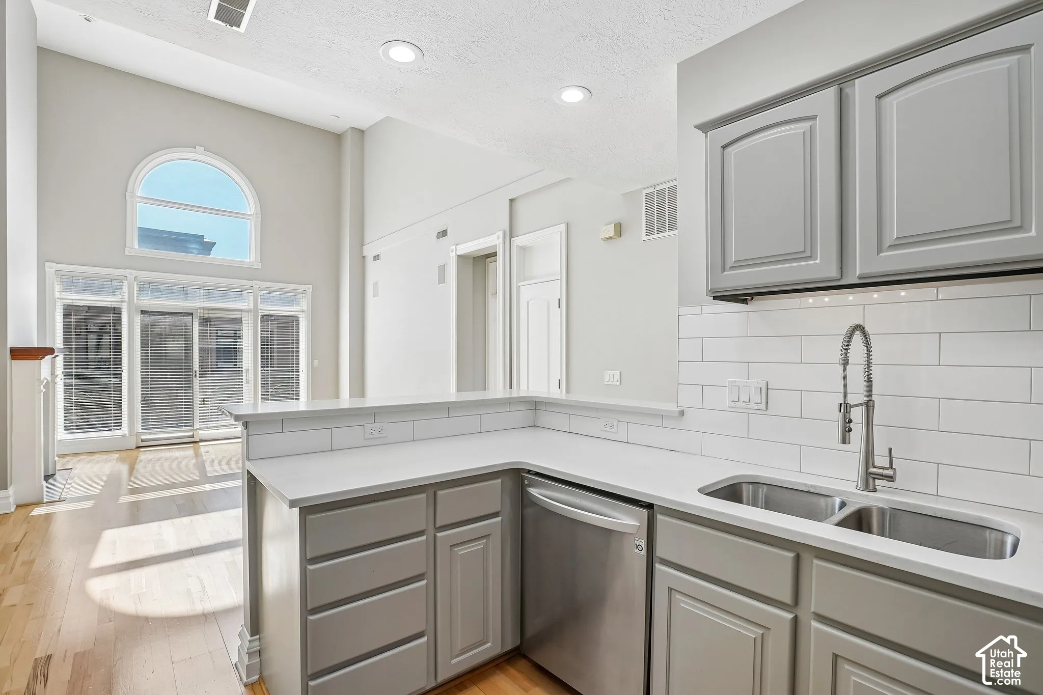 Kitchen featuring grey cabinetry, white countertops, subway tile backsplash, stainless steel under-mount double sink with pull-down faucet, and vaulted ceilings