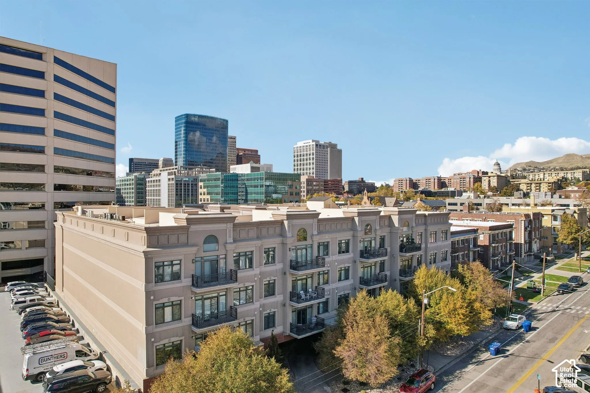 Multi-story masonry building featuring private balconies with wrought-iron railings and a prominent urban skyline backdrop