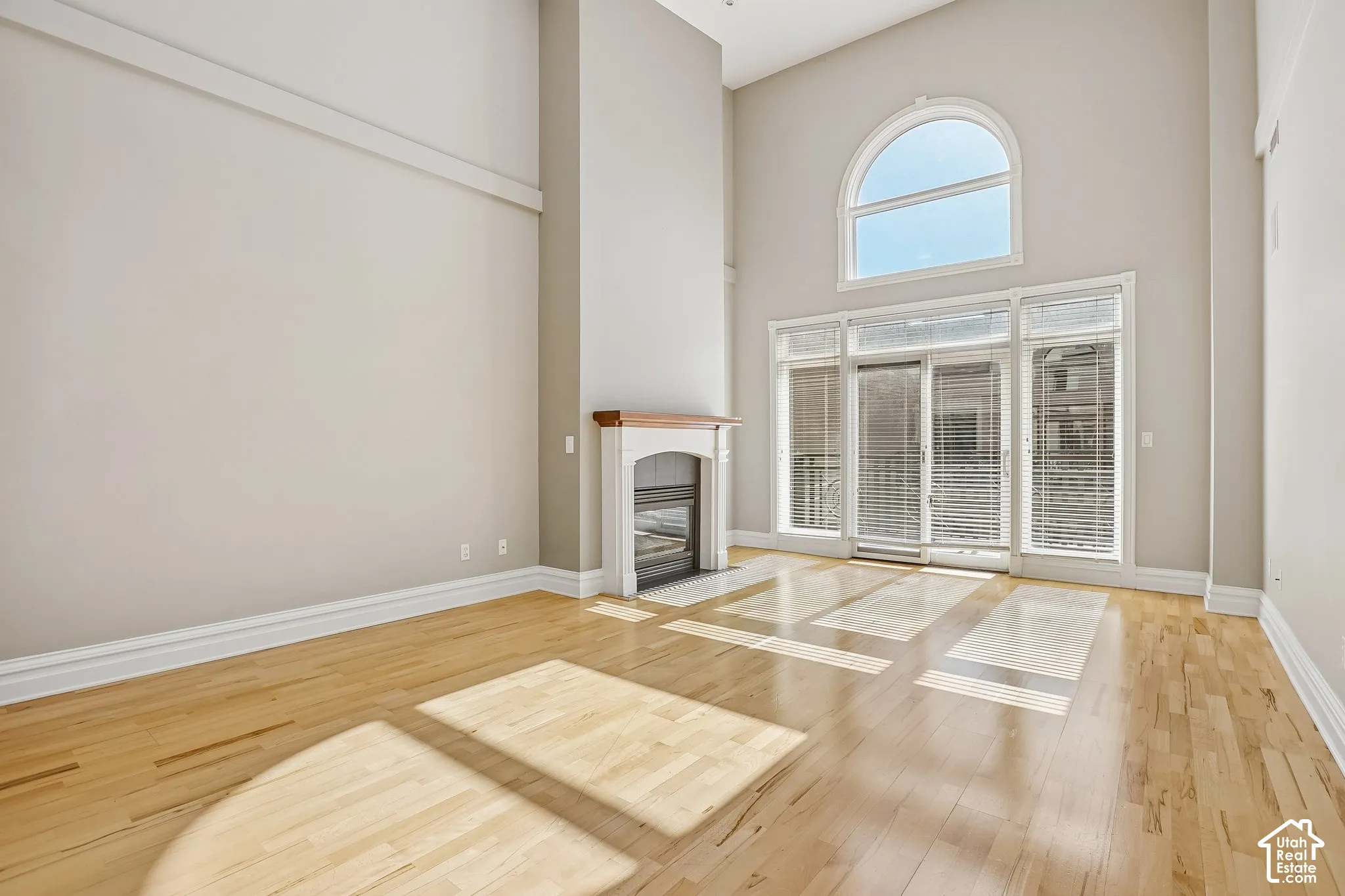 Vaulted ceilings, wood-finish flooring, fireplace with a mantel, arched window, and sliding glass door