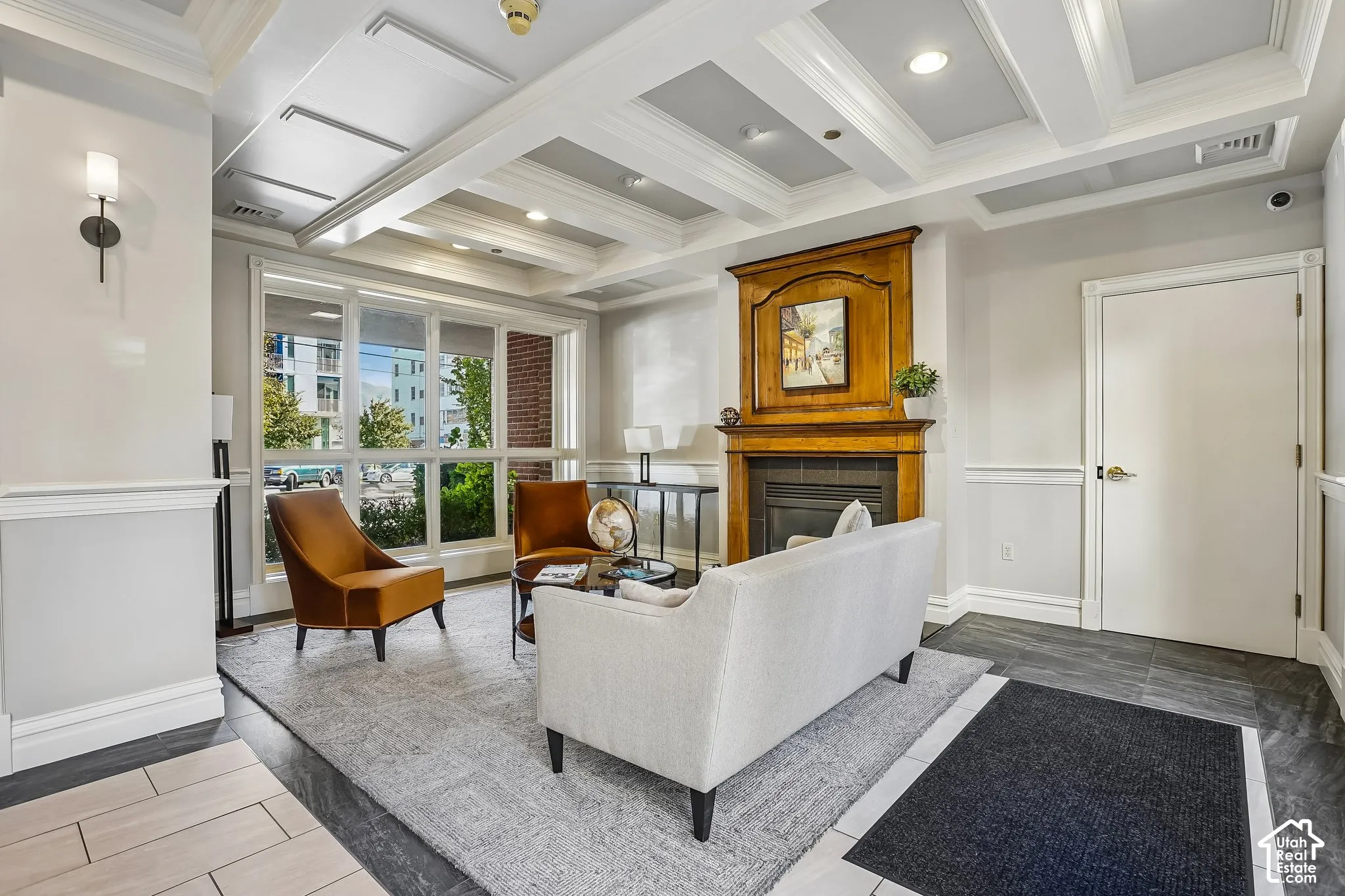 Coffered ceiling with integrated recessed lighting, decorative wood fireplace mantel, expansive multi-pane window assembly, wainscoting, and tile flooring