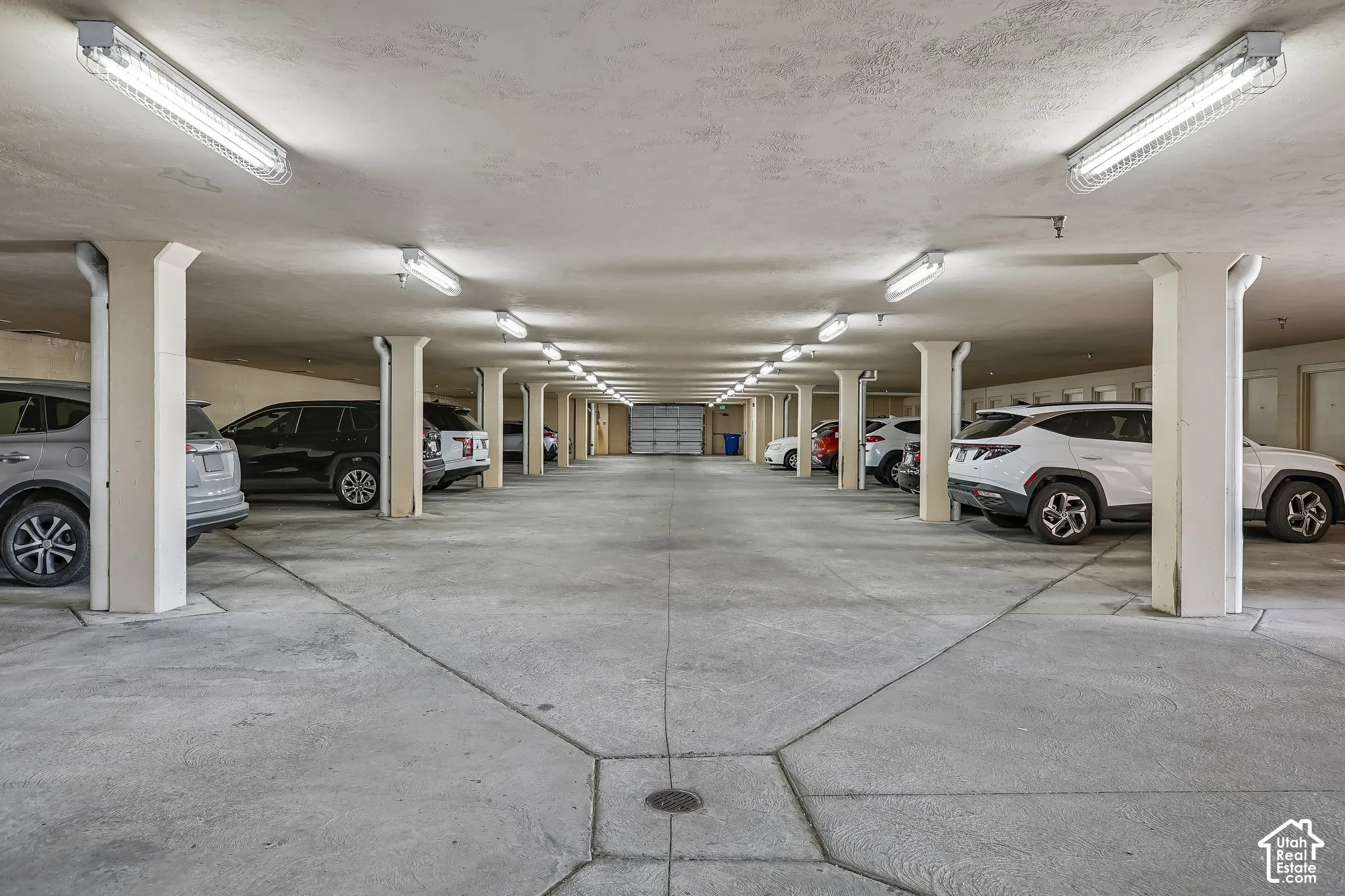 Covered parking structure featuring concrete flooring, overhead fluorescent lighting, and structural support pillars