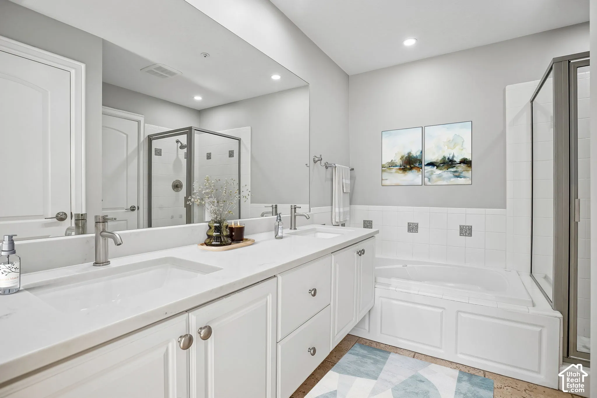 Double vanity with white cabinetry, light-toned countertops, undermount sinks, full-width wall mirror, and a tile-surround soaking tub