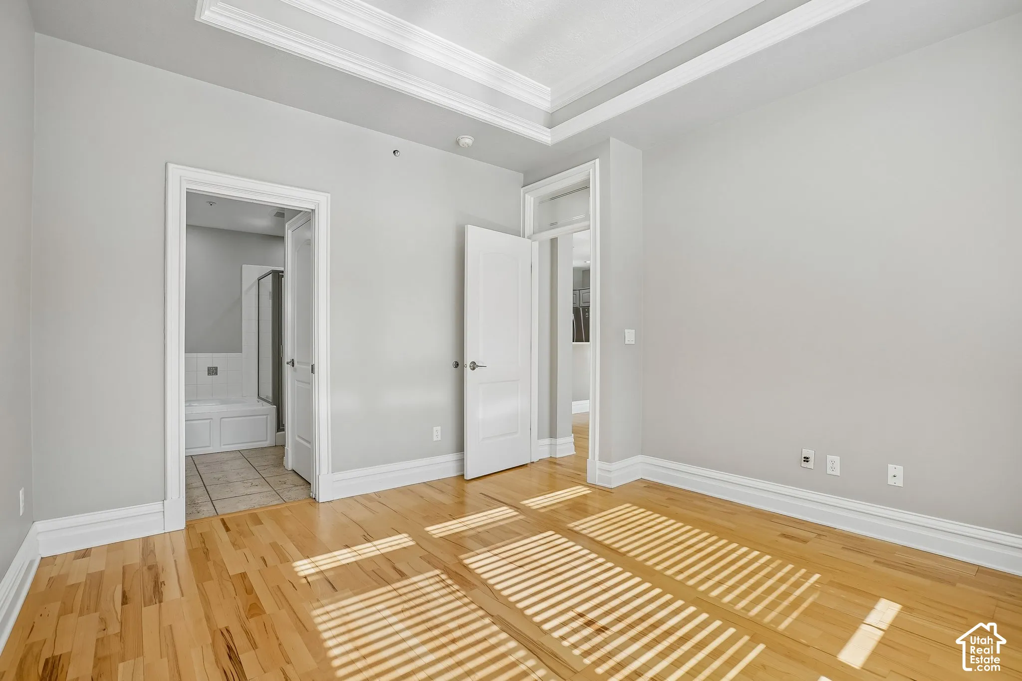 Room featuring light wood-finish flooring, a double-tray ceiling with crown molding, and neutral wall color