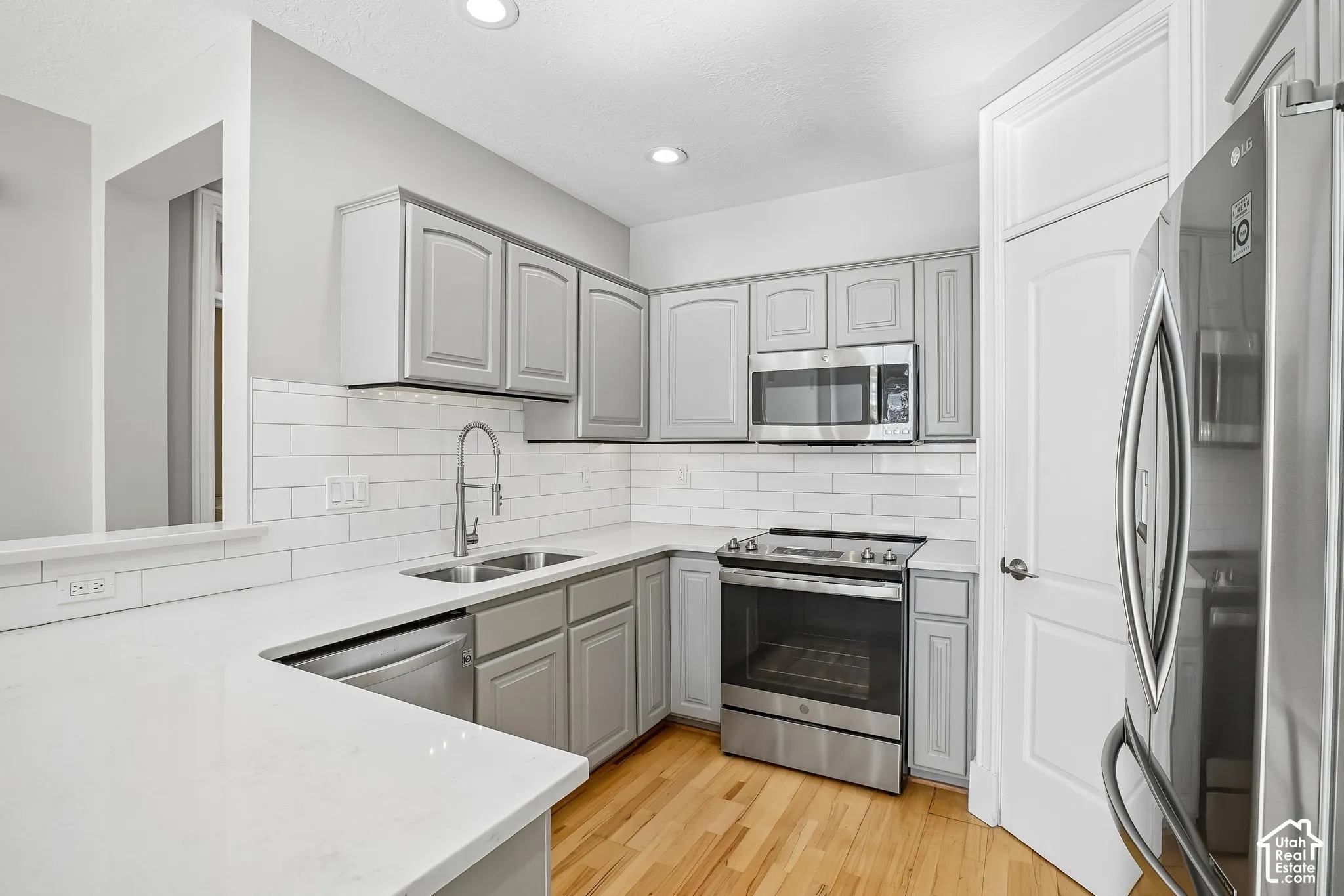 Kitchen featuring grey shaker-style cabinetry, white quartz countertops, white subway tile backsplash, stainless steel appliances, and wood-finish flooring