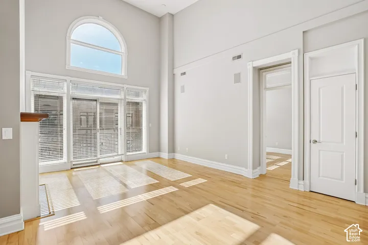 Double-height ceiling, arched window, wood-finish flooring, and multi-panel glass door