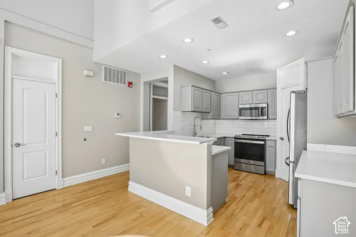Kitchen featuring wood-finish flooring, white solid-surface countertops, subway tile backsplash, recessed lighting, and stainless steel appliances