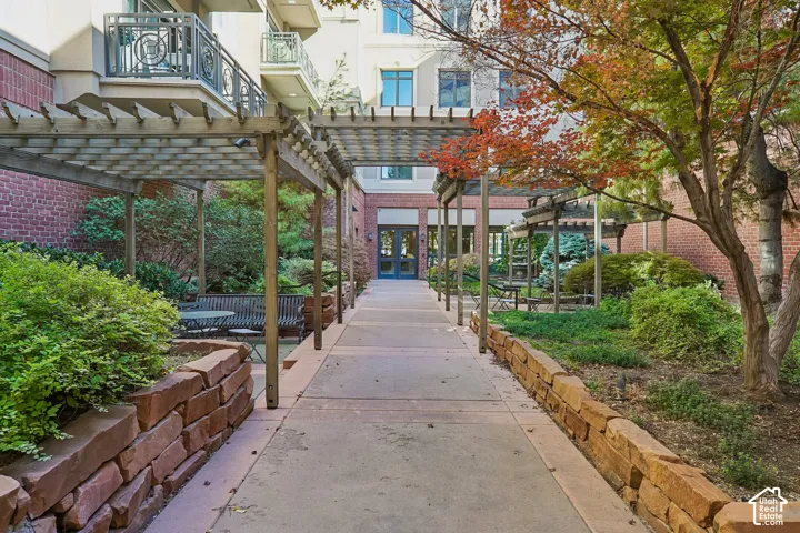 Courtyard walkway featuring timber pergolas, natural stone retaining walls, mature landscaping, and multi-story brick masonry exterior