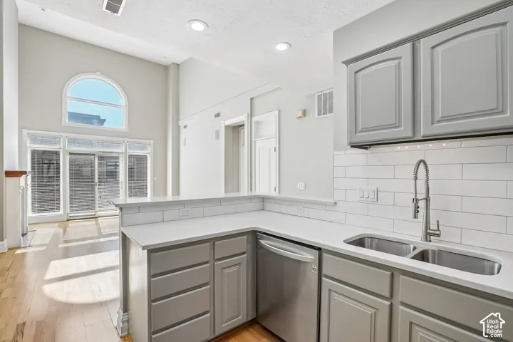 Kitchen featuring grey cabinetry, white countertops, subway tile backsplash, stainless steel under-mount double sink with pull-down faucet, and vaulted ceilings