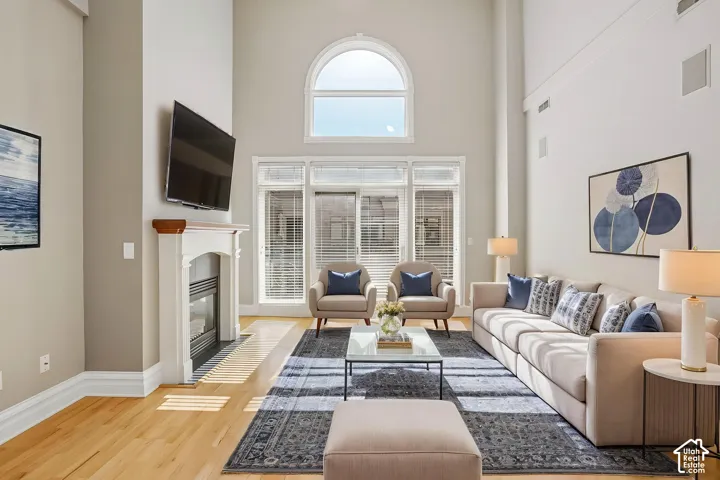 Living area featuring vaulted ceilings, wood-finish flooring, a central fireplace with a wood mantel, a prominent arched window, and large sliding glass doors
