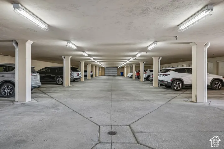 Covered parking structure featuring concrete flooring, overhead fluorescent lighting, and structural support pillars