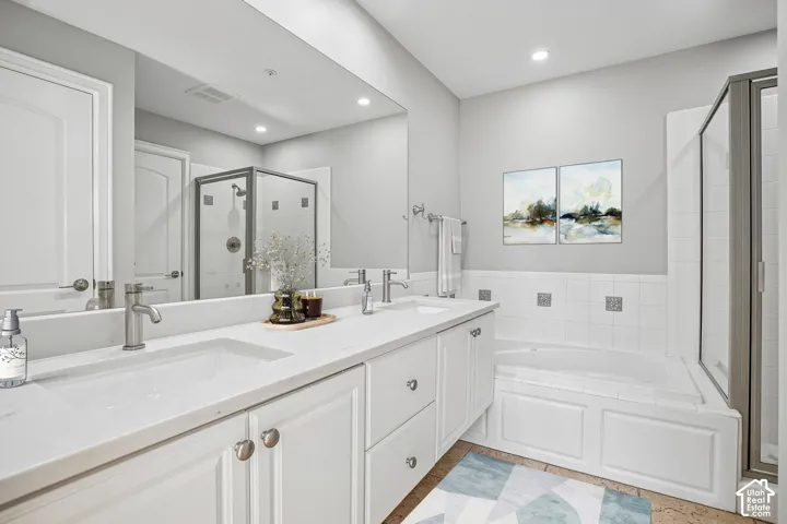 Double vanity with white cabinetry, light-toned countertops, undermount sinks, full-width wall mirror, and a tile-surround soaking tub