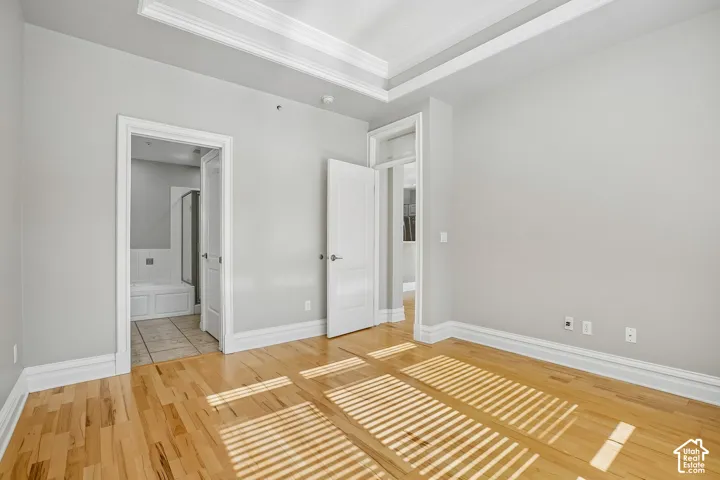 Room featuring light wood-finish flooring, a double-tray ceiling with crown molding, and neutral wall color