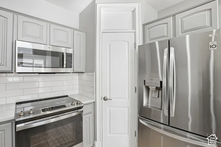 Kitchen featuring gray shaker-style cabinetry, stainless steel appliances, white subway tile backsplash, quartz countertops, and a full-height pantry door with crown molding