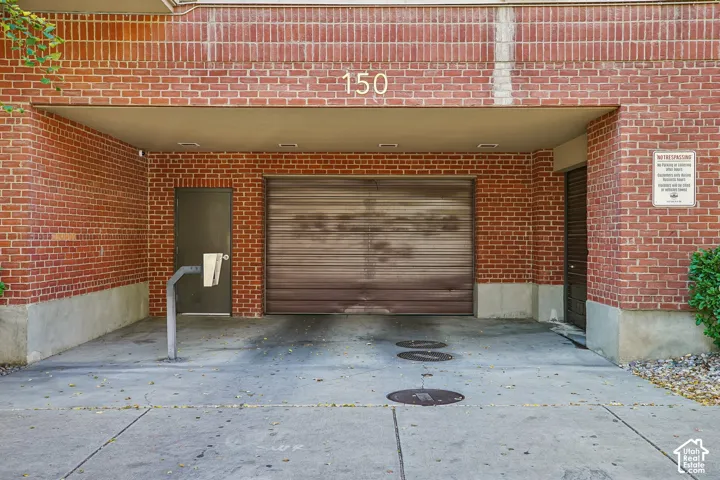 Brick exterior facade featuring a covered parking area with a rolling garage door, recessed lighting, and a separate service entrance