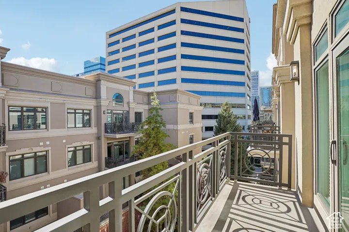 Private balcony featuring metal decorative railing, exterior wall-mounted lighting, and glass paneled door entry