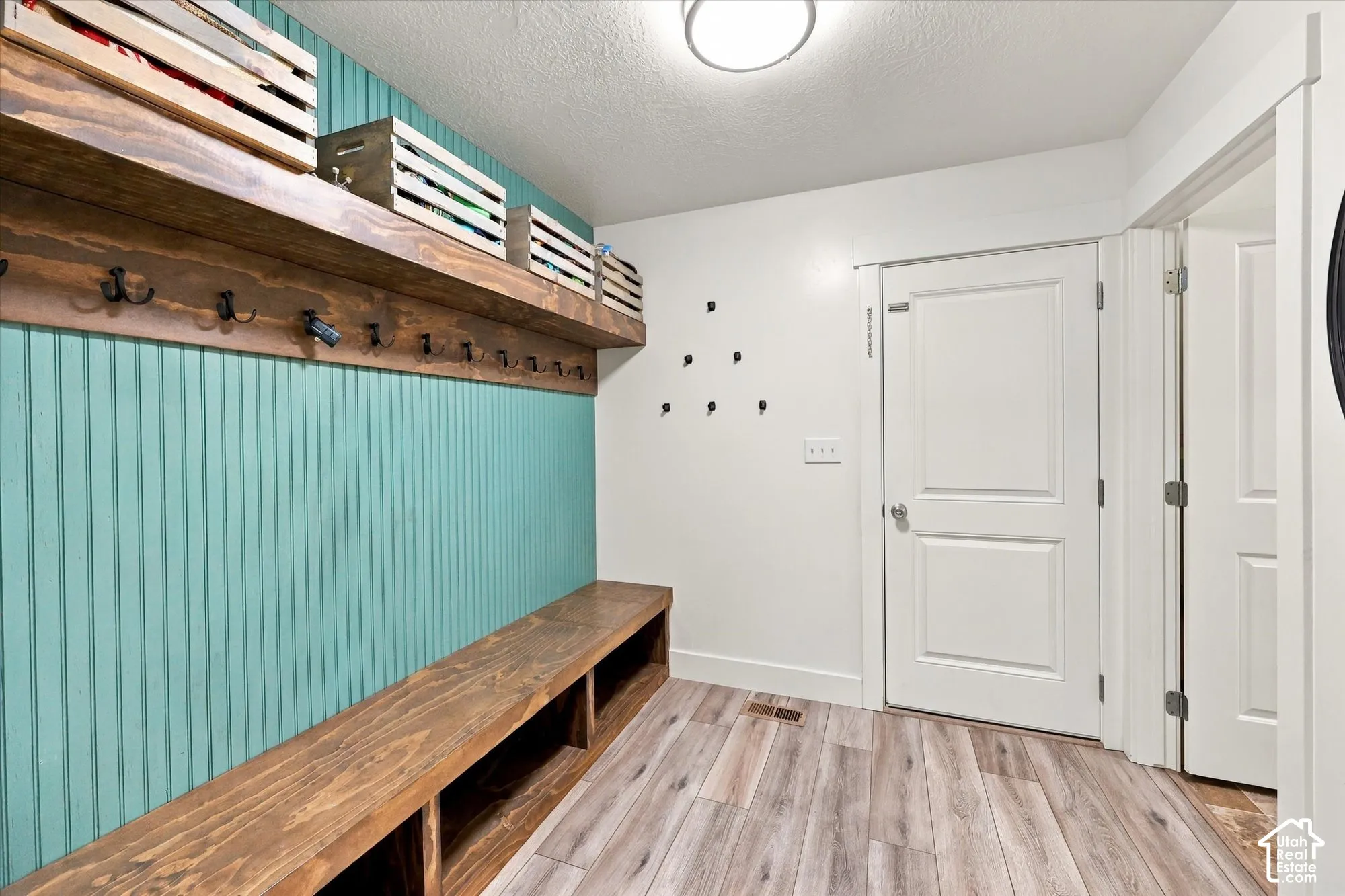 Beadboard wall paneling, built-in wooden bench with open lower shelving, wall-mounted wooden shelf with iron coat hooks, and wood-finish flooring