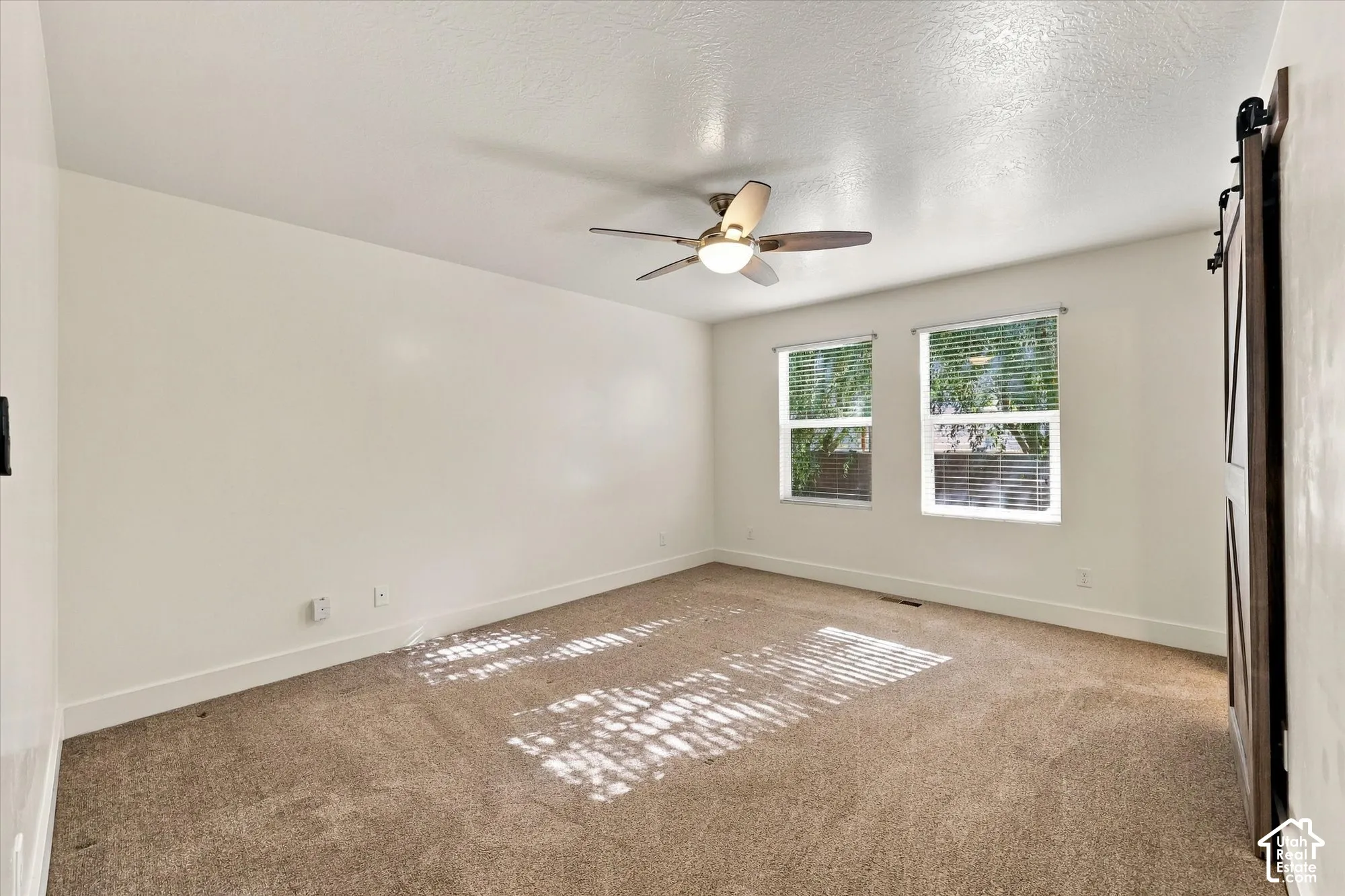 Room featuring carpeted flooring, dual windows, a ceiling fan with integrated lighting, and a sliding barn-style door