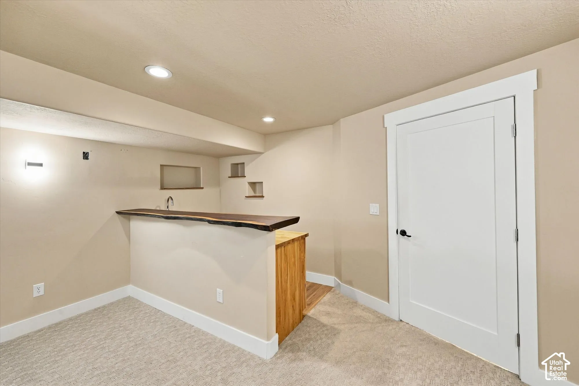 Built-in bar featuring a natural edge wood countertop, recessed wall niches, and wood-finish cabinetry, complemented by recessed ceiling lighting and a white shaker-style interior door