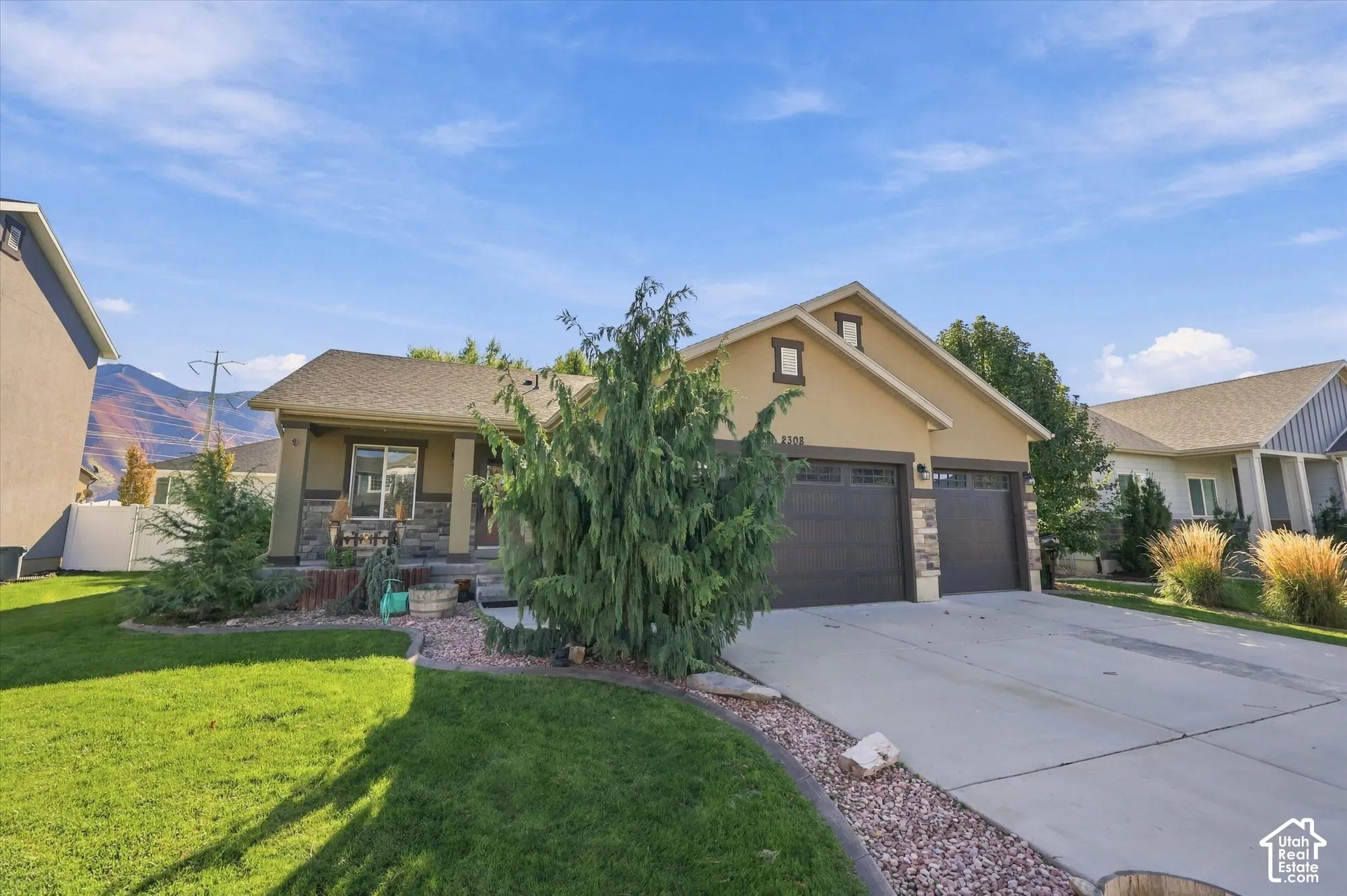 Exterior featuring a stucco facade with stone veneer accents, a covered front entryway, an attached three-car garage, and a manicured front lawn