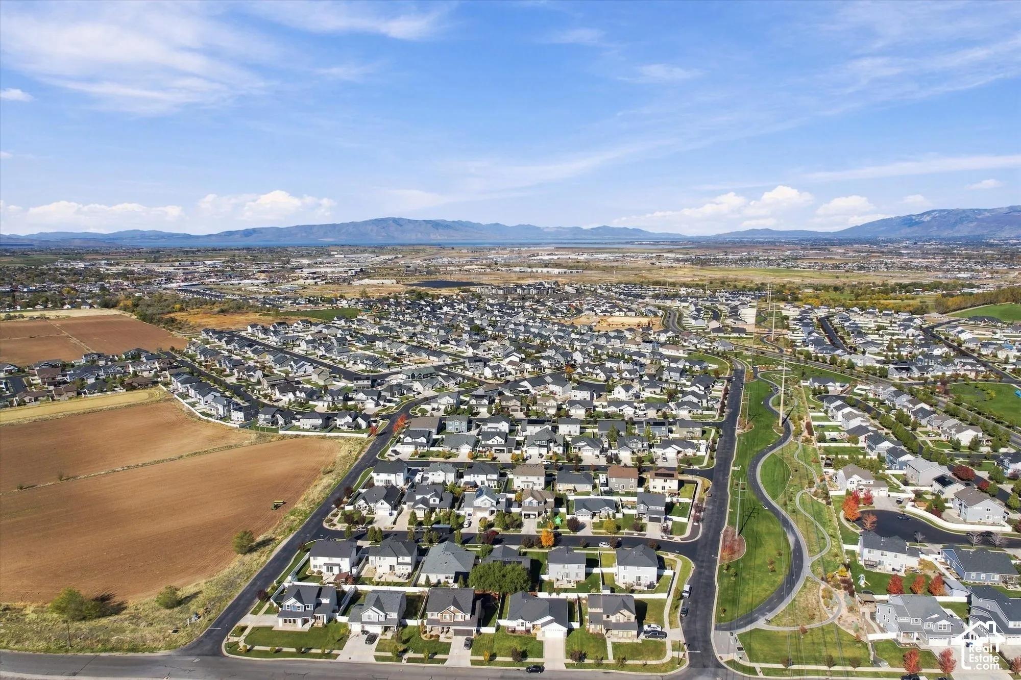 Aerial perspective of a suburban neighborhood featuring paved roadways, manicured green space, pedestrian pathways, and distant mountain scenery