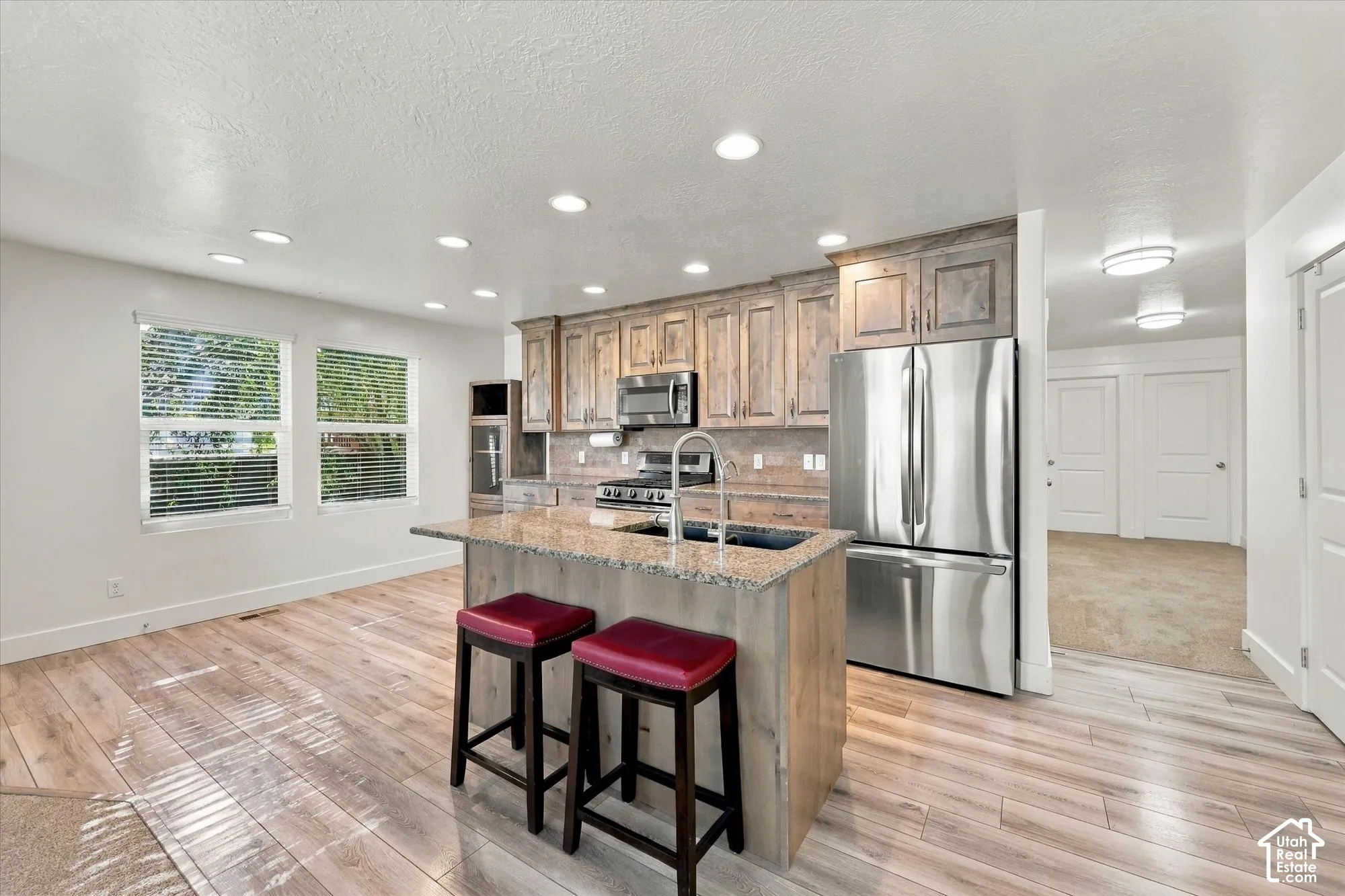 Kitchen featuring wood-finish cabinetry, stone countertops, a center island with a stainless steel sink, stainless steel appliances, and wood-finish flooring