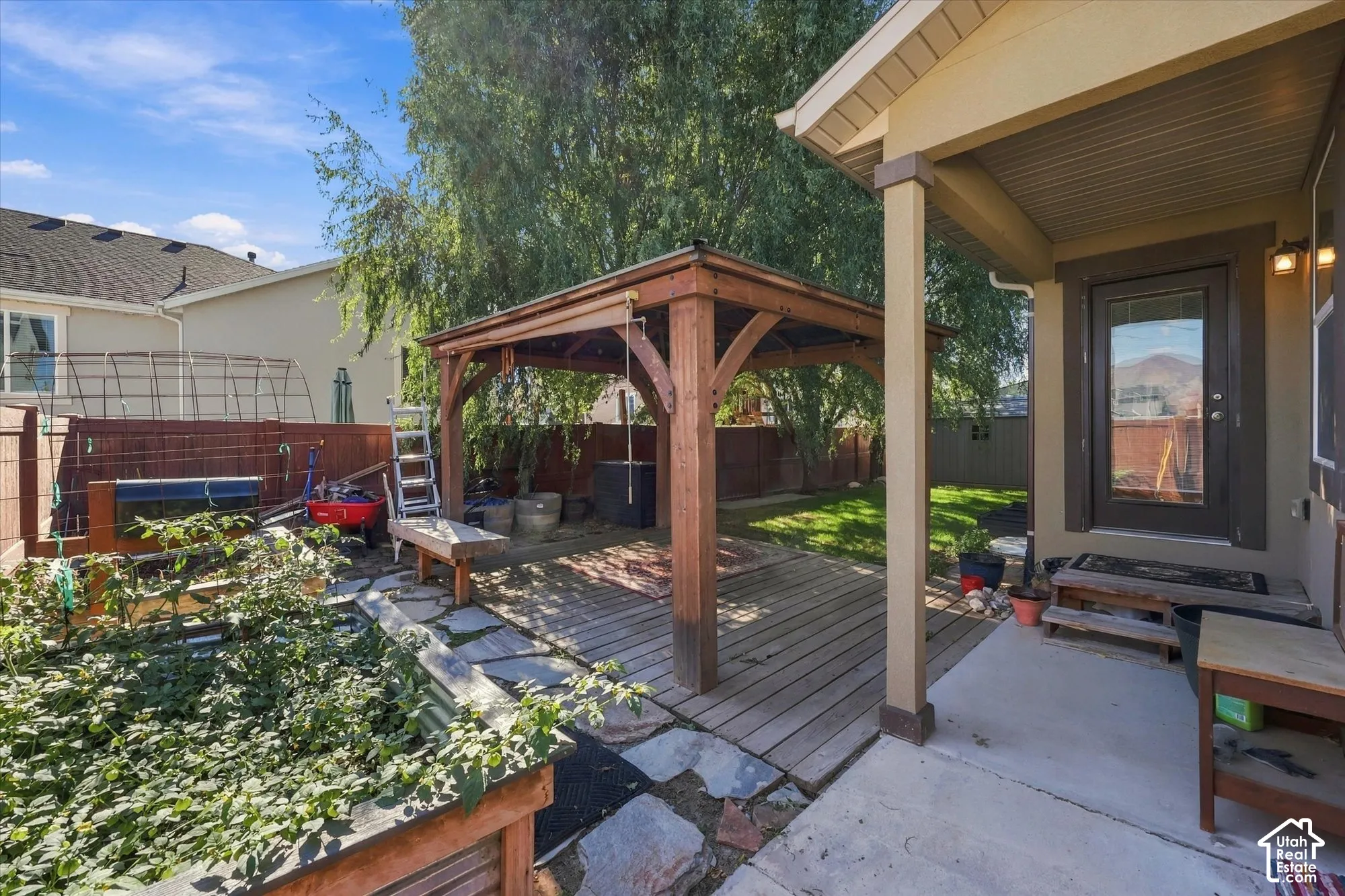 Outdoor living space featuring a covered patio, wood-frame gazebo, flagstone hardscaping, and raised garden beds enclosed by perimeter fencing