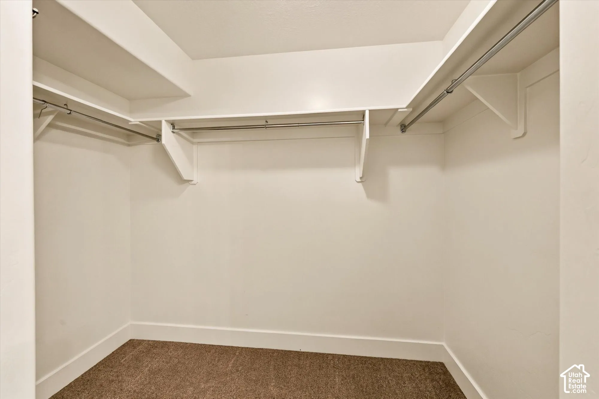 Walk-in closet featuring tiered white shelving and integrated metal garment rods