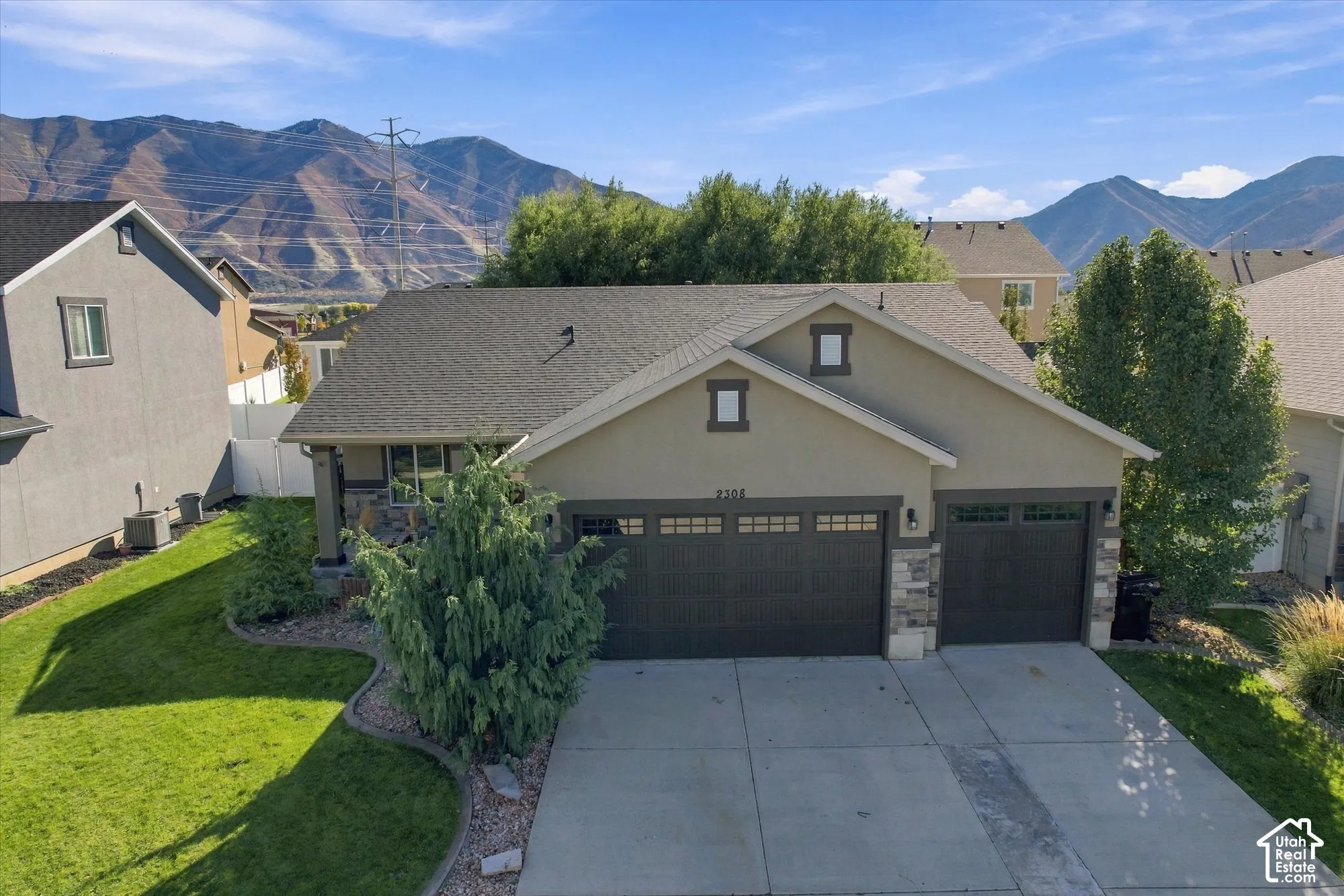 Single-family residence featuring a composite shingle roof, stone veneer accents, three-car garage with transom windows, and mountain backdrop