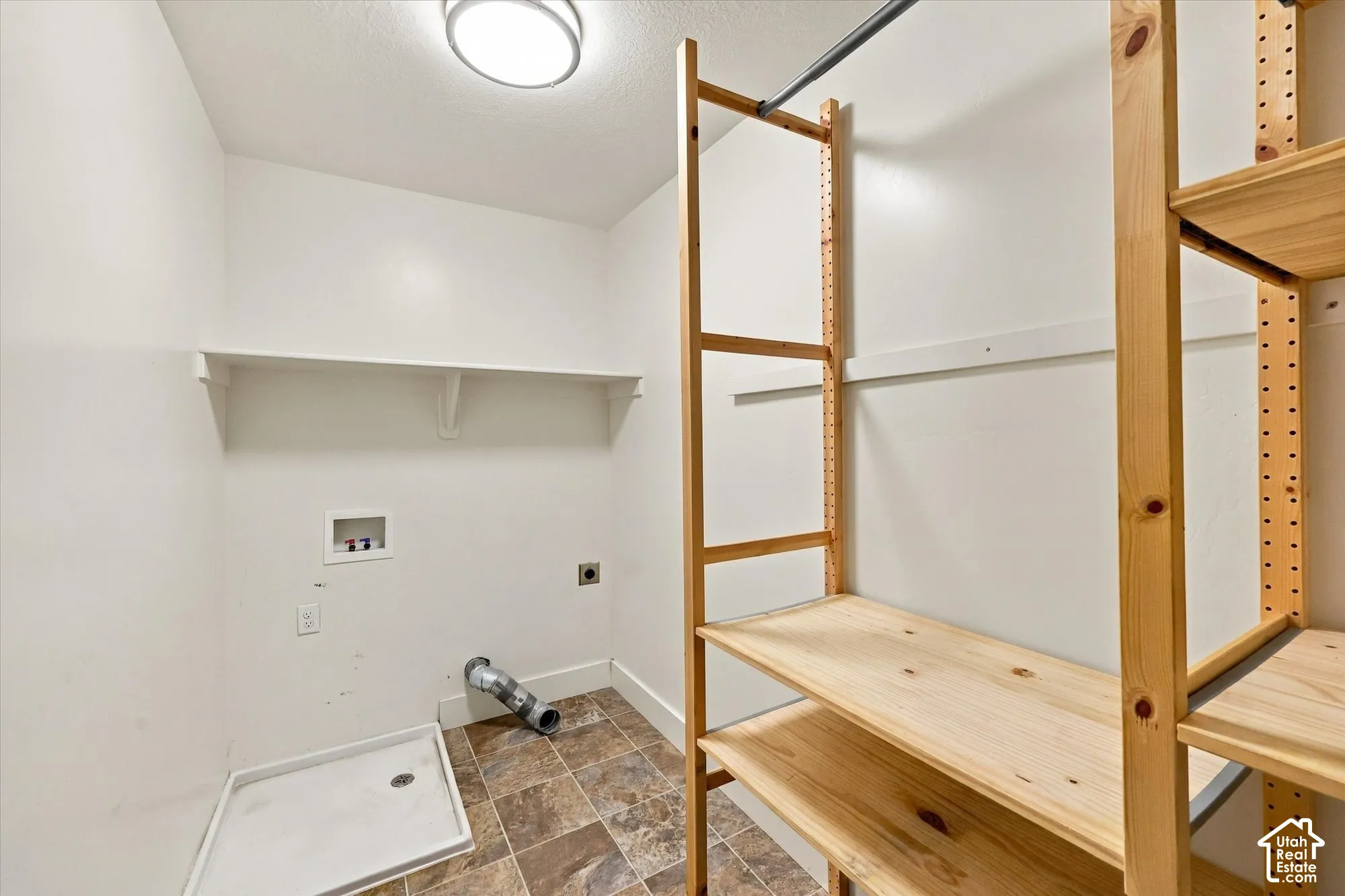 Utility space featuring tile flooring, built-in wooden shelving, a recessed wall-mounted shelf, and dedicated water and dryer hookups