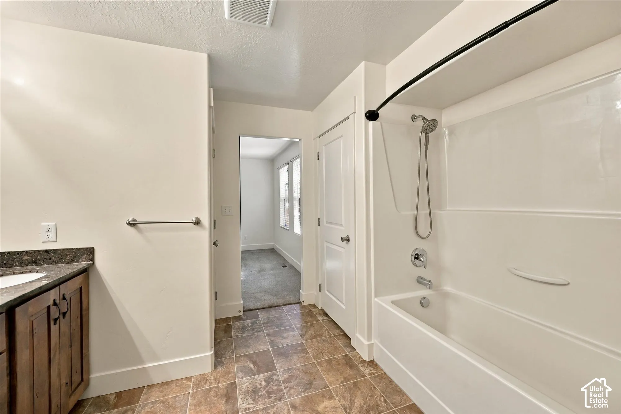 Bathroom featuring dark-stained cabinetry, stone-finish countertop, ceramic tile flooring, and a combined tub and shower enclosure with a wall-mounted faucet