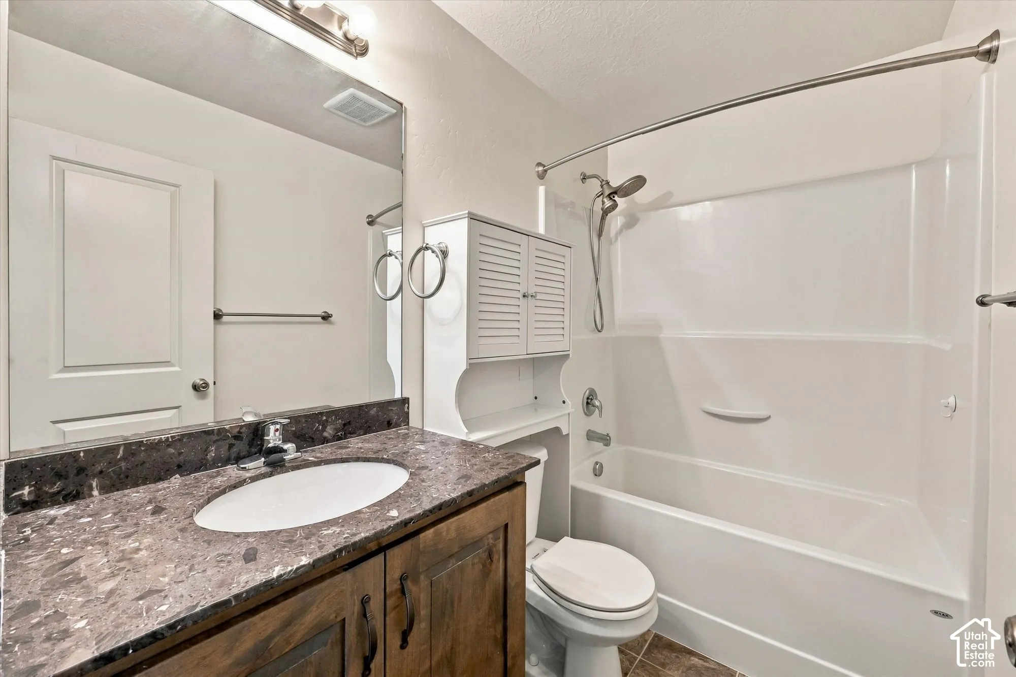 Bathroom featuring a stone-look countertop, wood-finish vanity cabinetry, undermount oval sink, and a combination tub-and-shower enclosure with a white surround