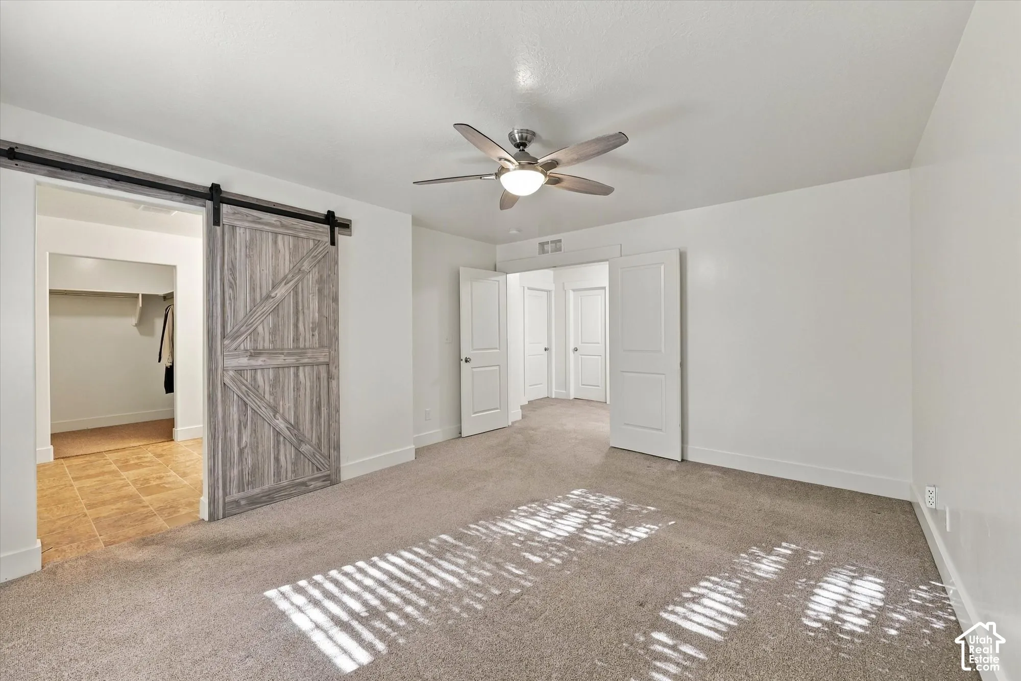 Interior space featuring a sliding wood-finish barn door, neutral carpeting, ceiling fan with integrated lighting, and white multi-panel interior doors