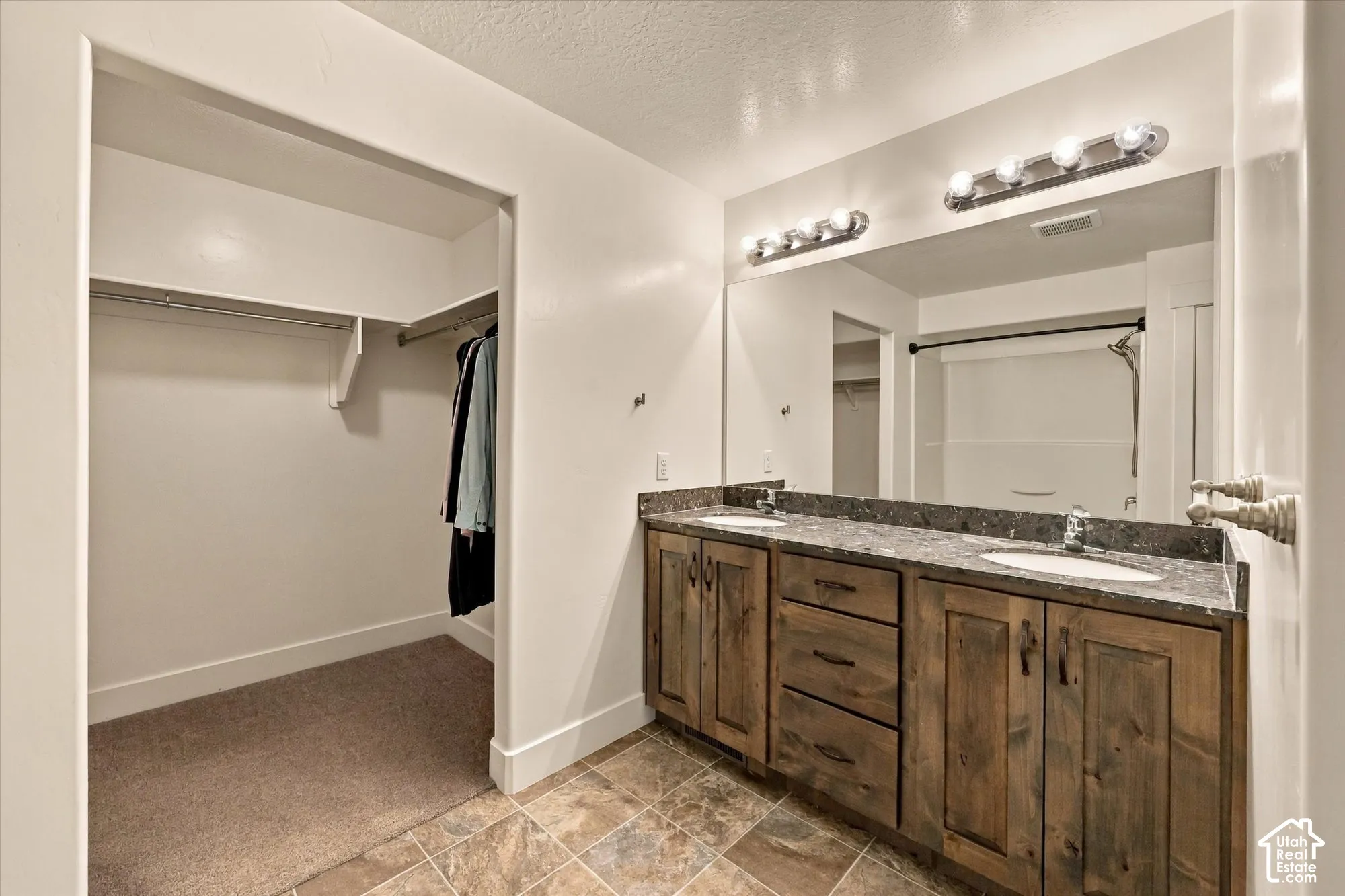 Dual-sink vanity with stone-finish countertop and rustic wood cabinetry, full-width vanity mirror, six-light fixture, and built-in walk-in closet with shelving