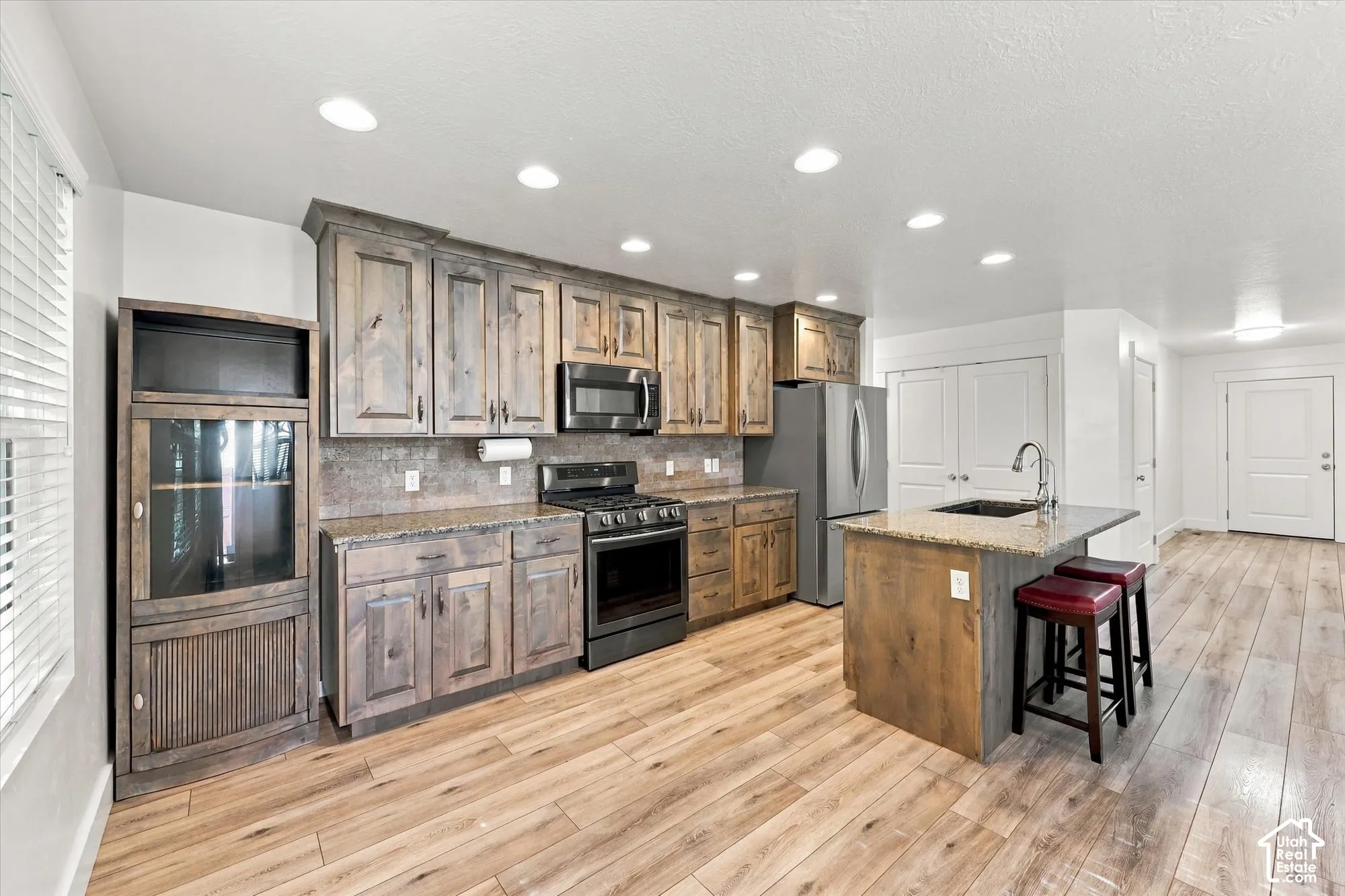 Kitchen featuring stained wood cabinetry, stone-surface countertops, wood-finish flooring, stainless steel appliances, and a central island