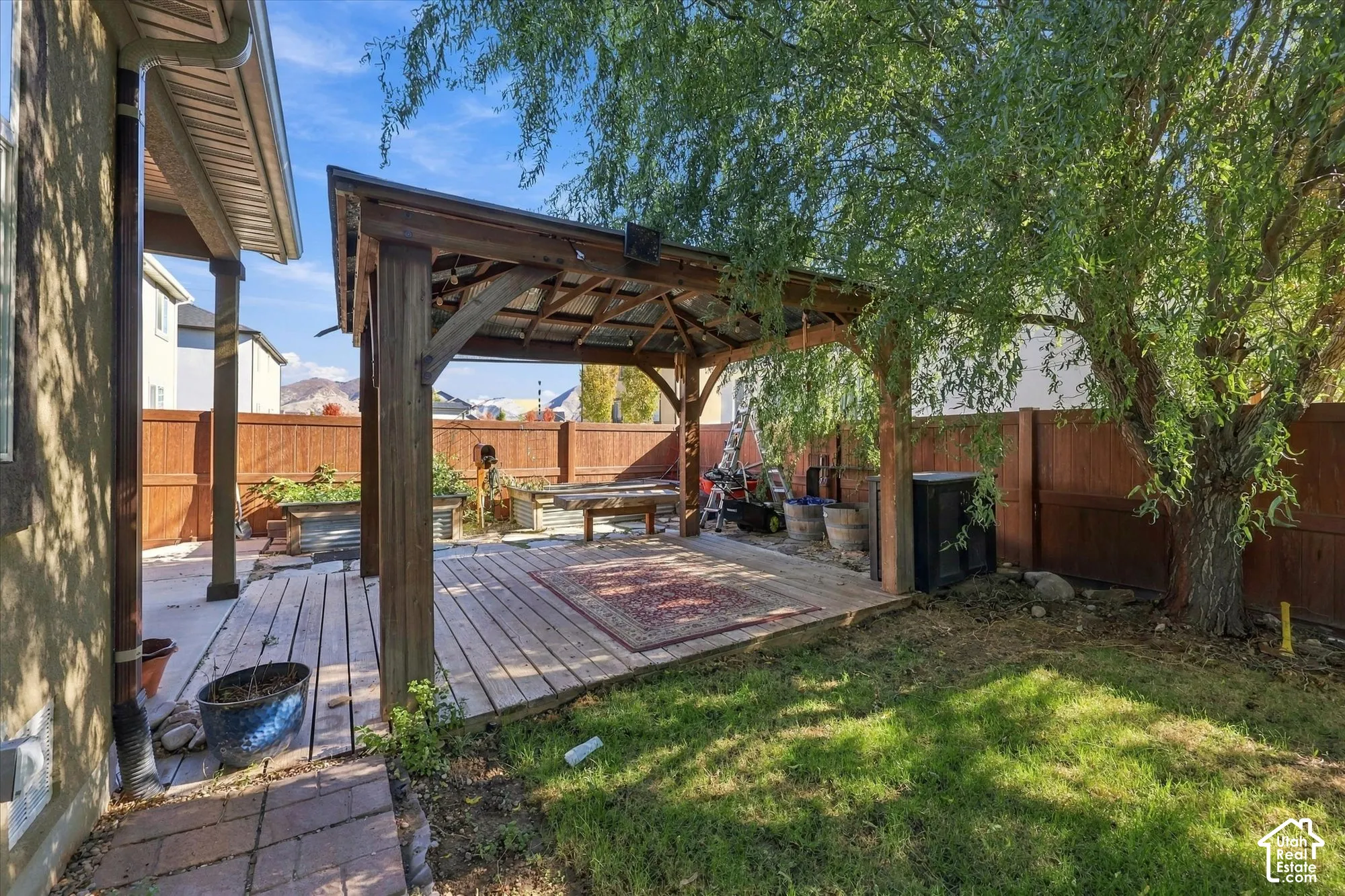 Outdoor living area featuring a wood-framed gazebo with a metal roof, tiered wood decking, a brick paver pathway, and a perimeter privacy fence