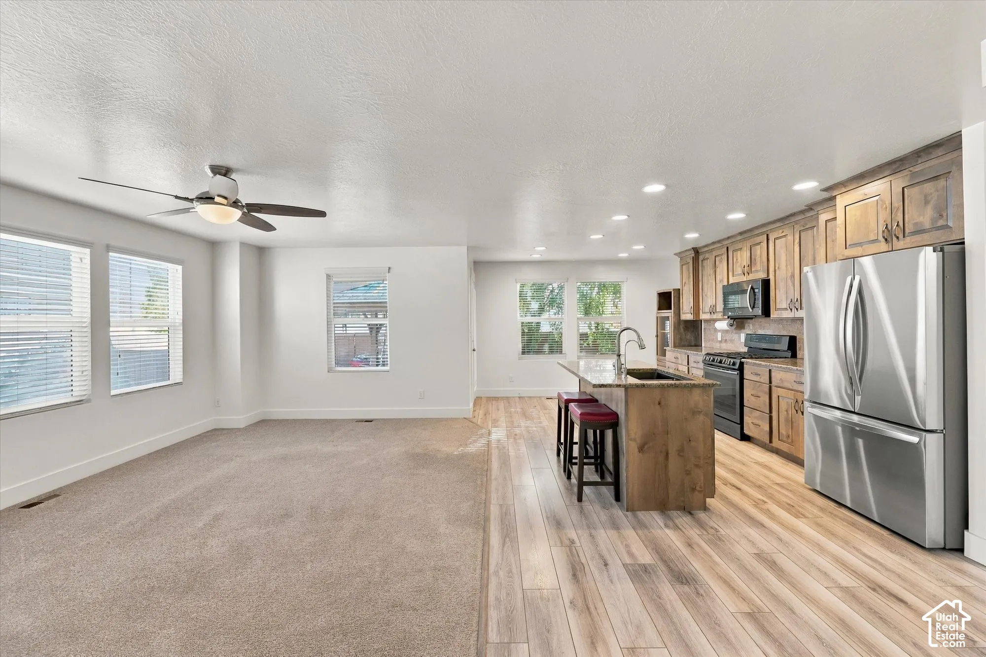 Kitchen featuring wood-finish cabinetry, stone-surface center island with a basin sink, stainless steel appliances, recessed ceiling lighting, and wood-finish flooring