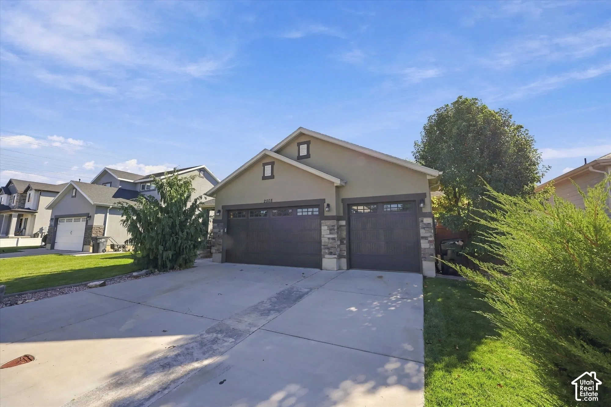 Exterior featuring a three-car garage, stone veneer accents, multi-pane garage door windows, and a concrete driveway