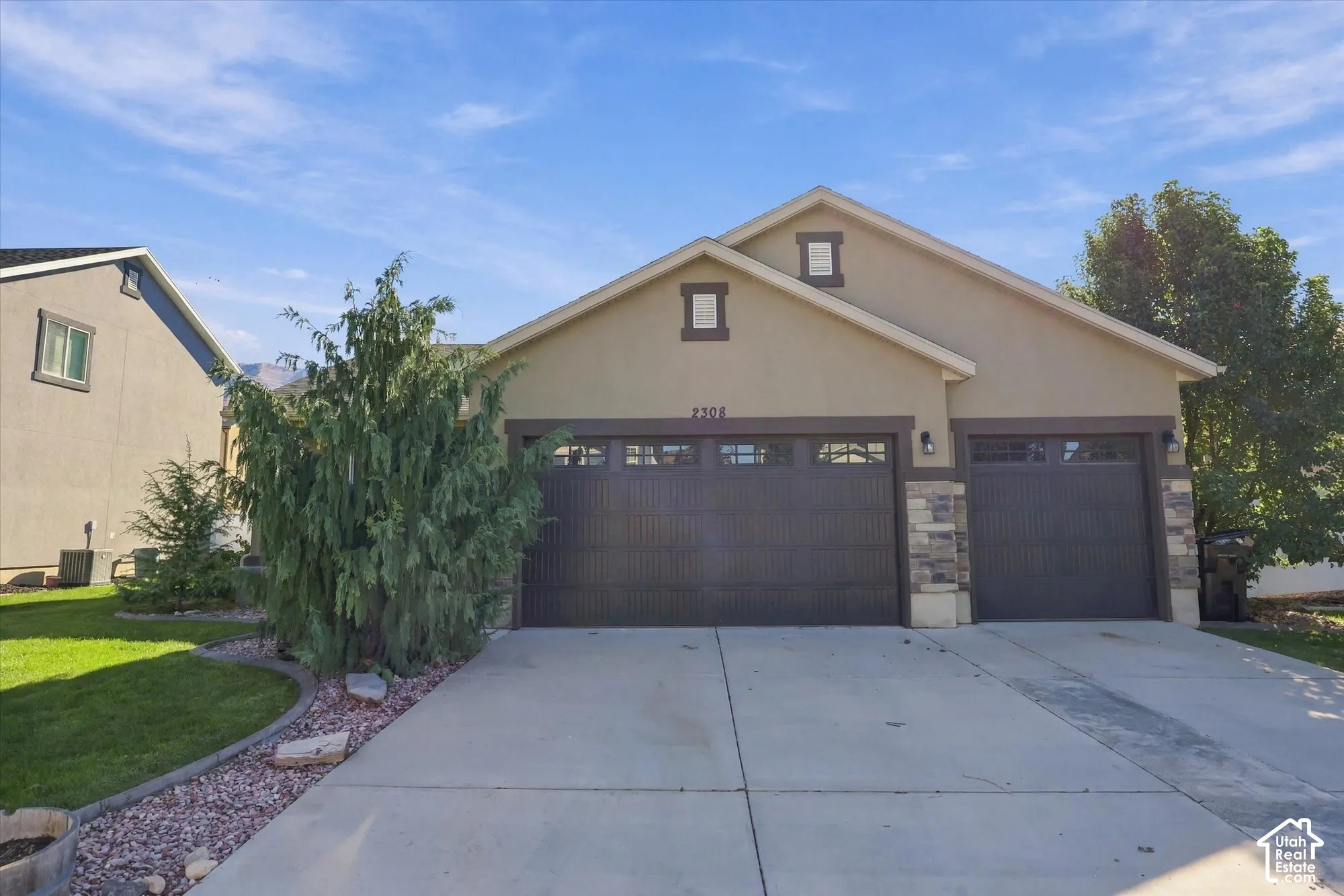 Stucco exterior featuring a three-car garage, stone veneer accents, concrete driveway, and gabled roofline