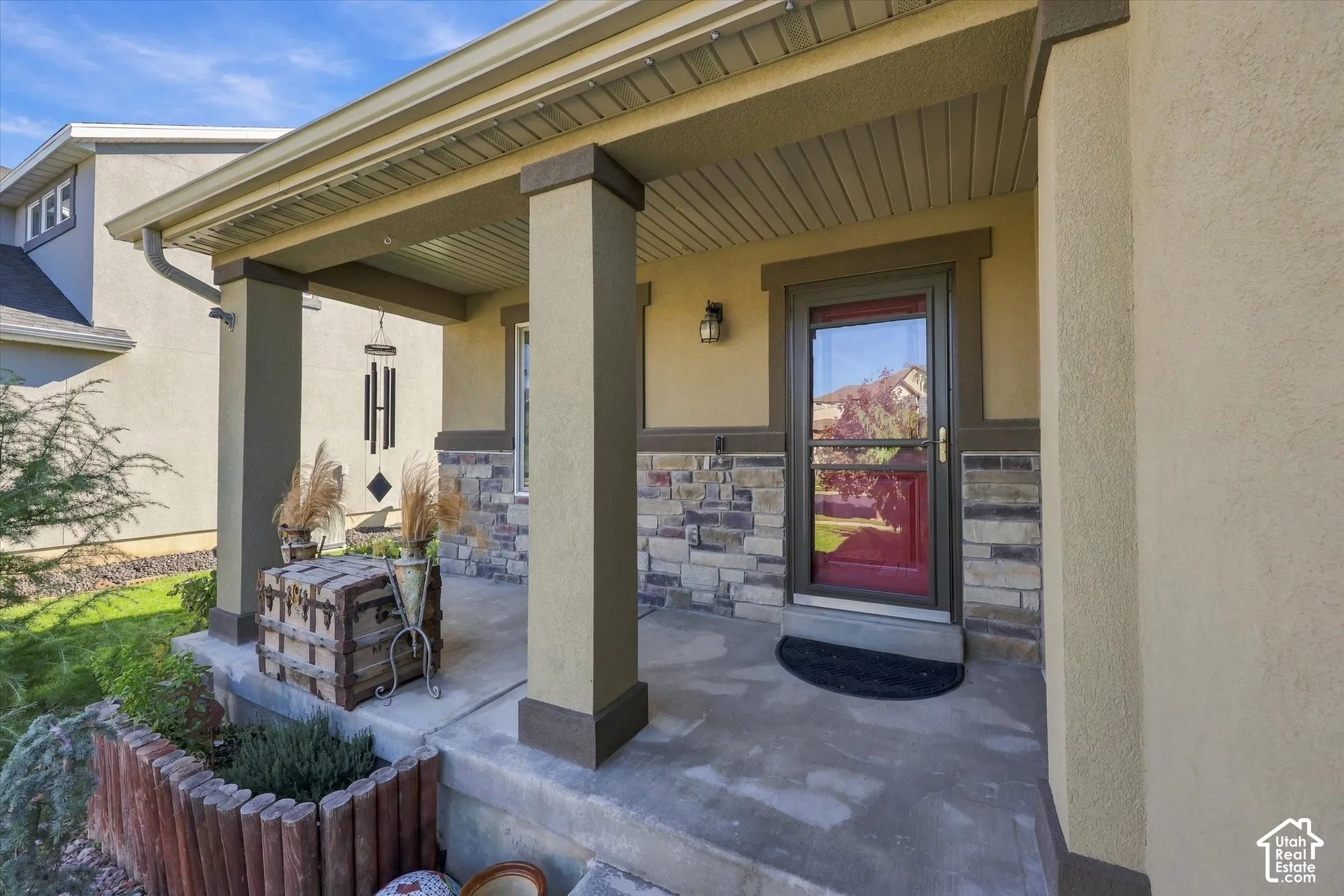 Covered front porch featuring stone veneer accents, structural pillars, and a glass-paneled entry door
