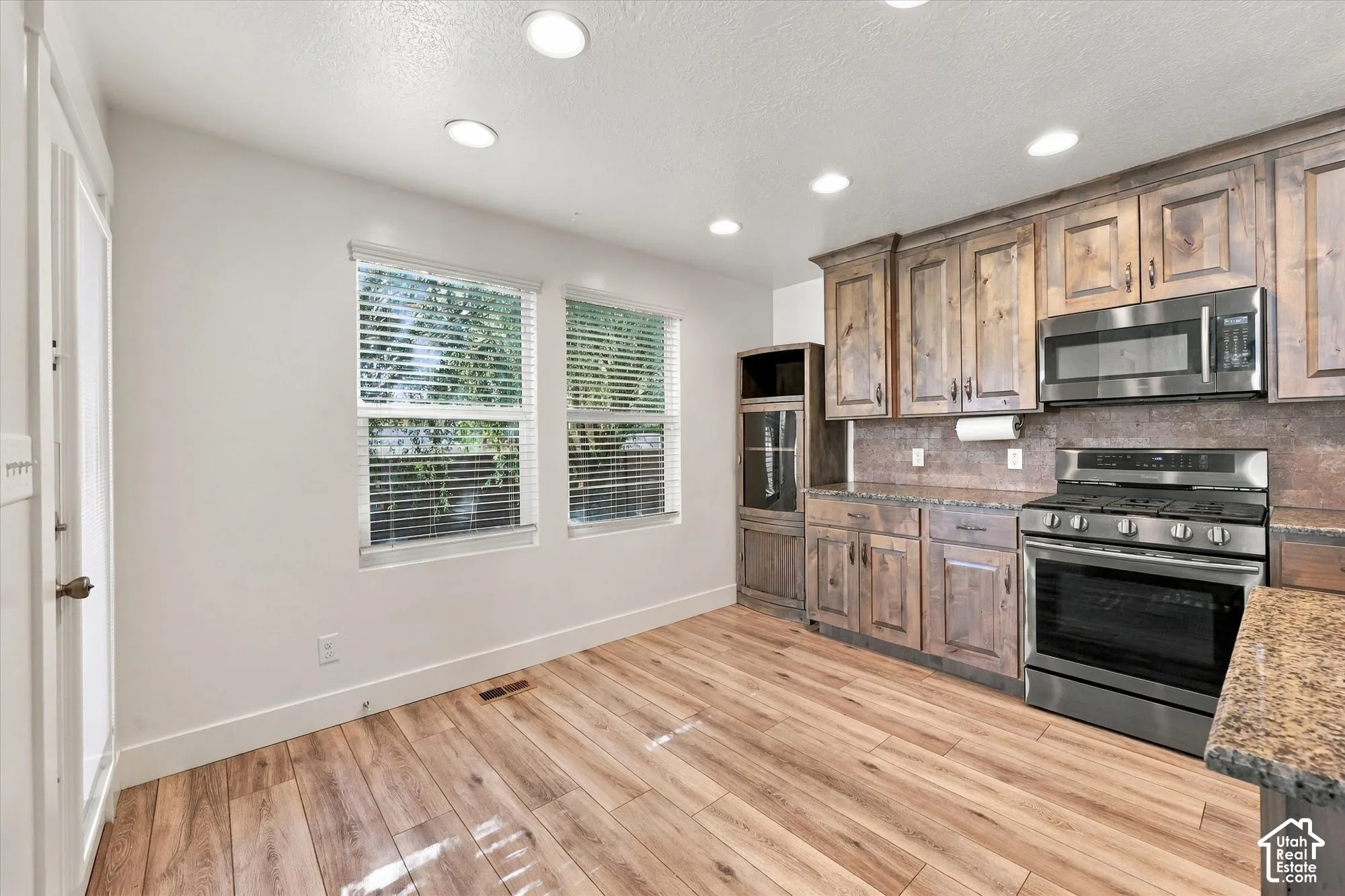 Kitchen featuring wood-finish flooring, rustic-style cabinetry, stainless steel appliances, stone-surface countertops, and recessed lighting